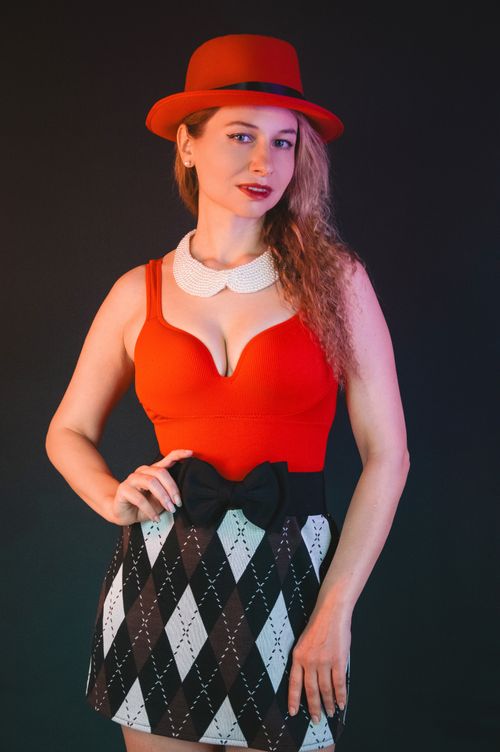 Free Stylish woman posing confidently in a red hat and patterned dress against a dark background. Stock Photo