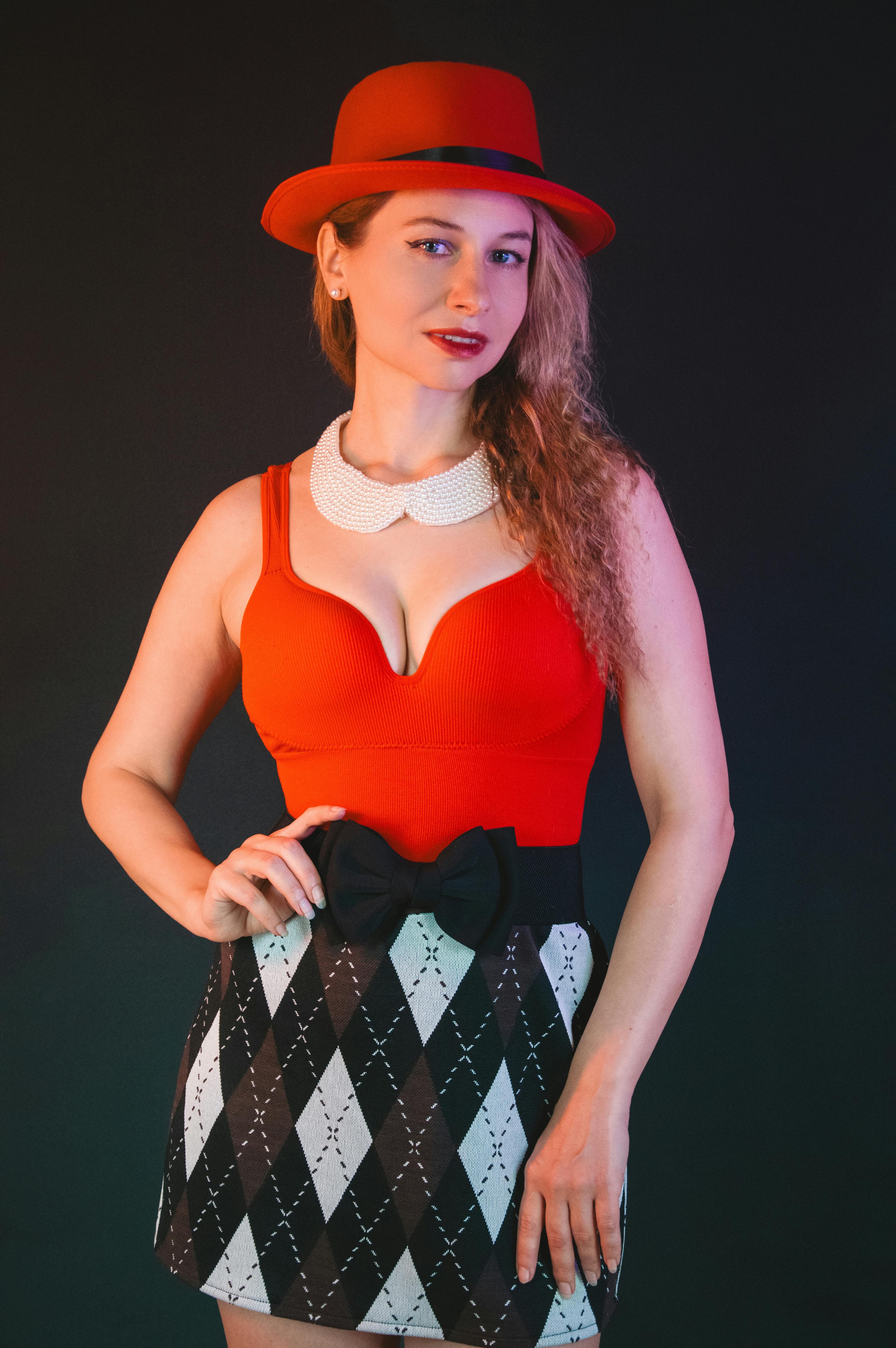 gratis Een stijlvolle vrouw poseert vol zelfvertrouwen met een rode hoed en een jurk met patroon tegen een donkere achtergrond. Stockfoto