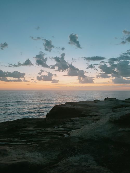Free Beautiful sunset over the ocean with dramatic clouds and rocky shoreline in view. Stock Photo