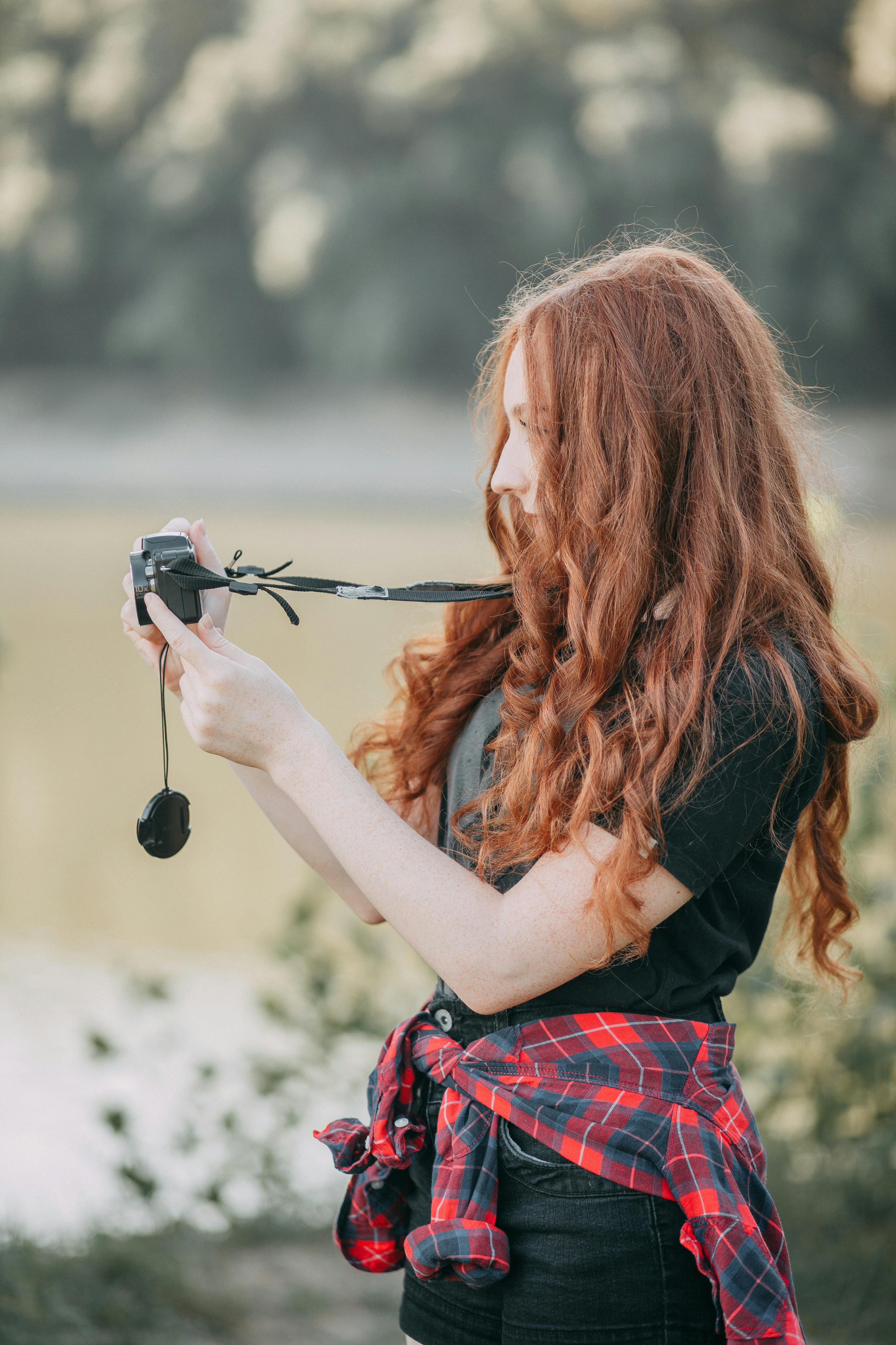 一名年轻的红发女子在户外手持相机，捕捉大自然的美丽