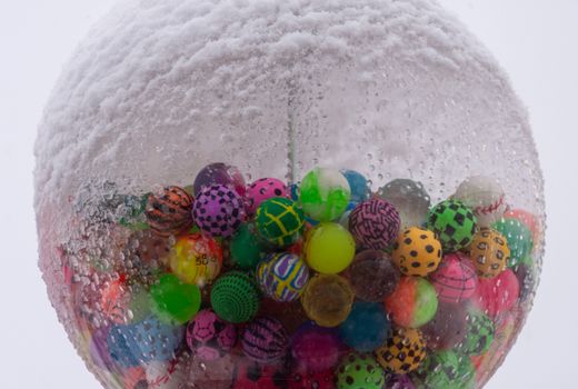 A snow-covered gumball machine with vibrant balls creates a whimsical winter scene.