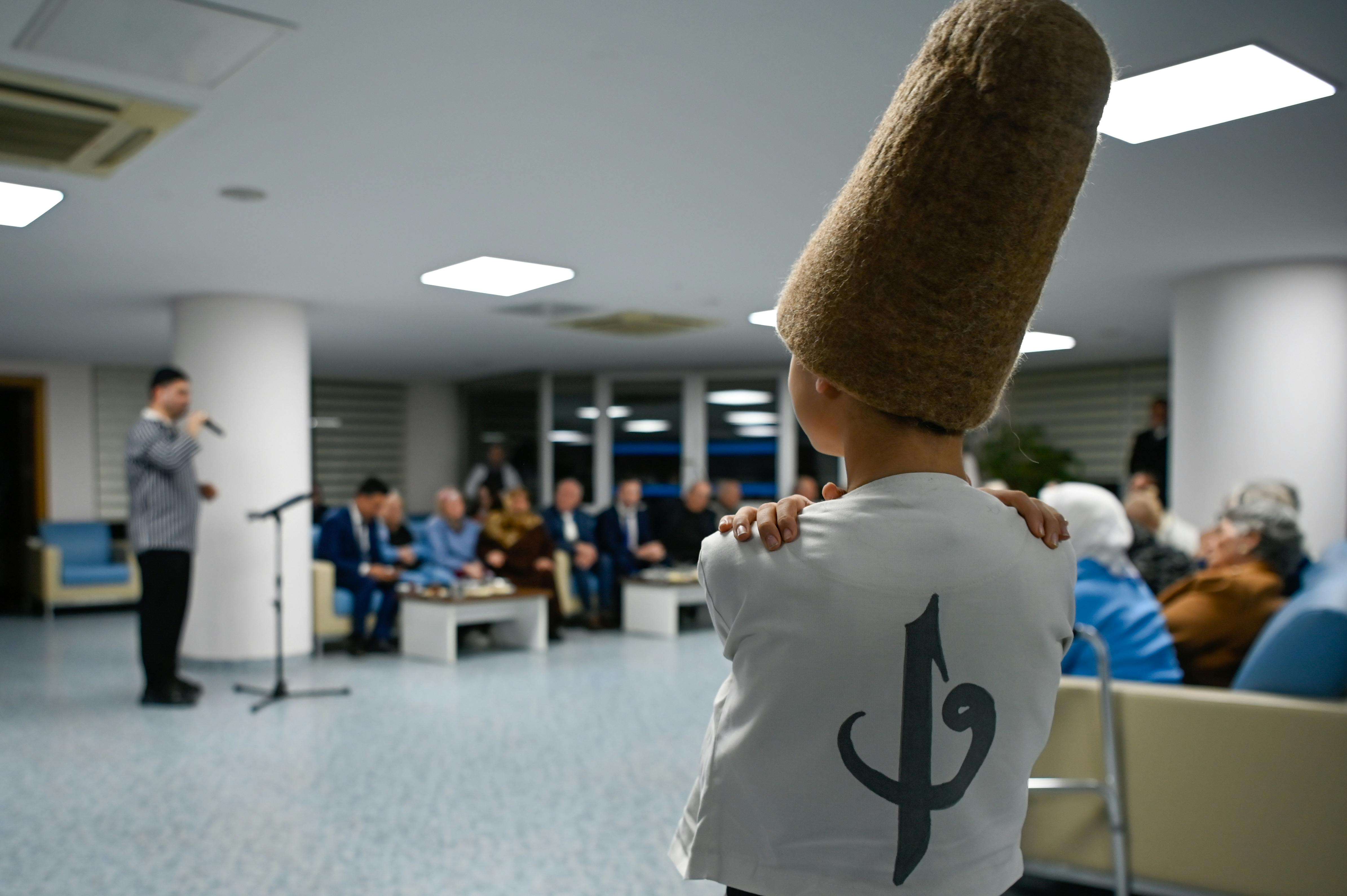 ingyenes Egy hagyományos öltözéket viselő fiatal fiú egy előadót figyel egy beltéri rendezvényen, közönség jelenlétében. Stockfotó