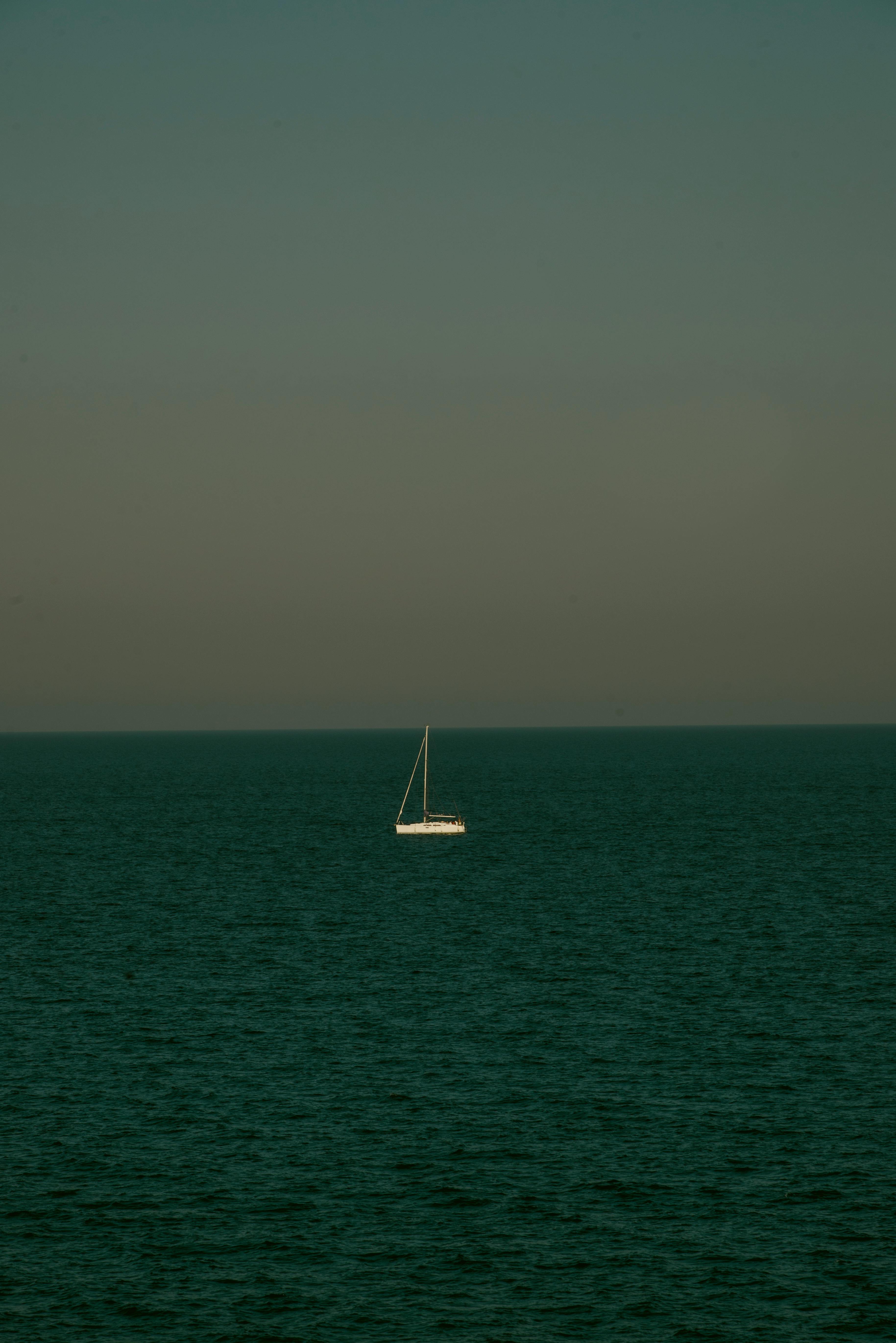 ingyenes Egy magányos vitorlás sodródik a nyílt tengeren a tiszta ég alatt, békét és magányt idézve. Stockfotó