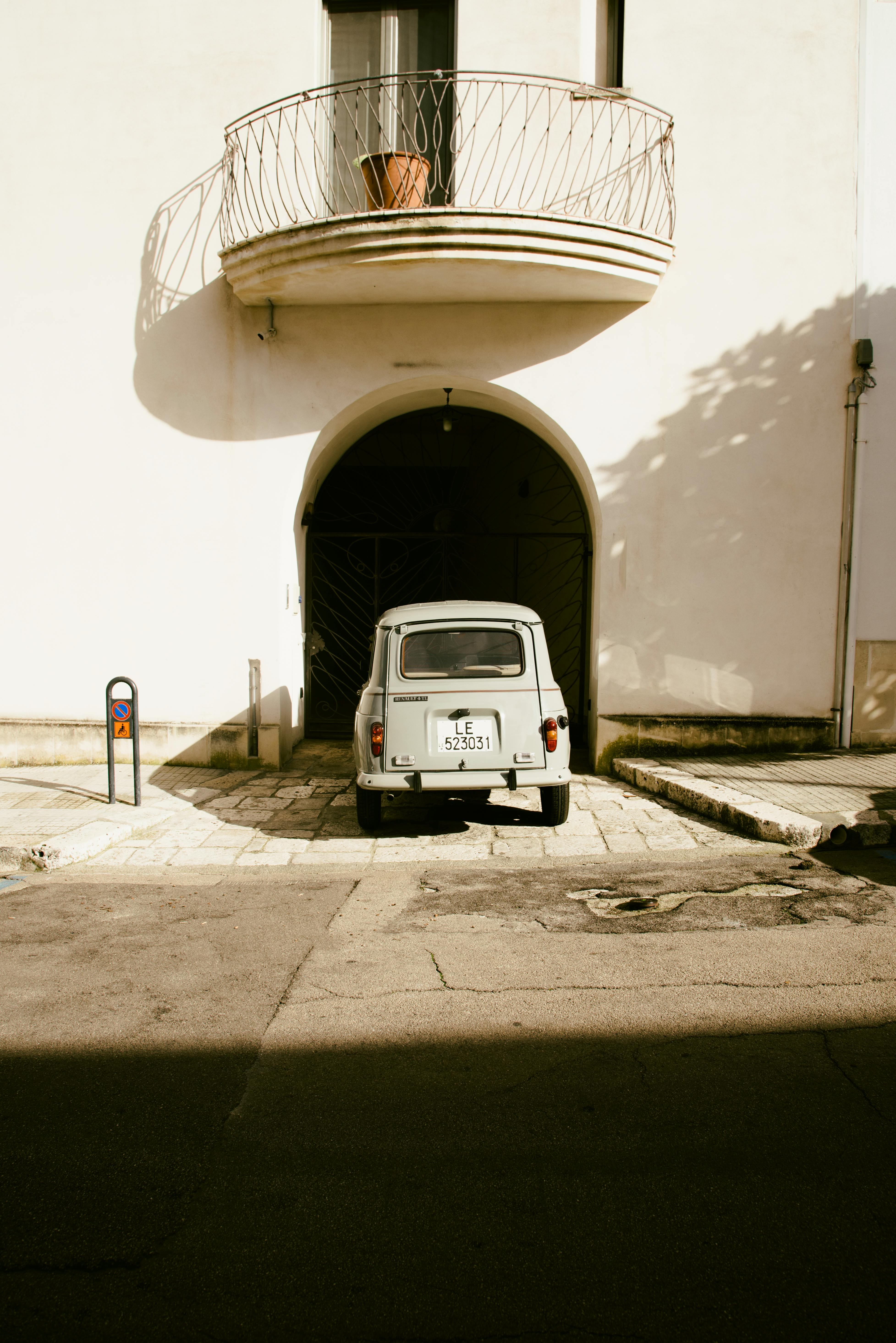 grátis Veículo antigo estacionado sob um arco com uma varanda acima, em uma rua ensolarada. Foto profissional