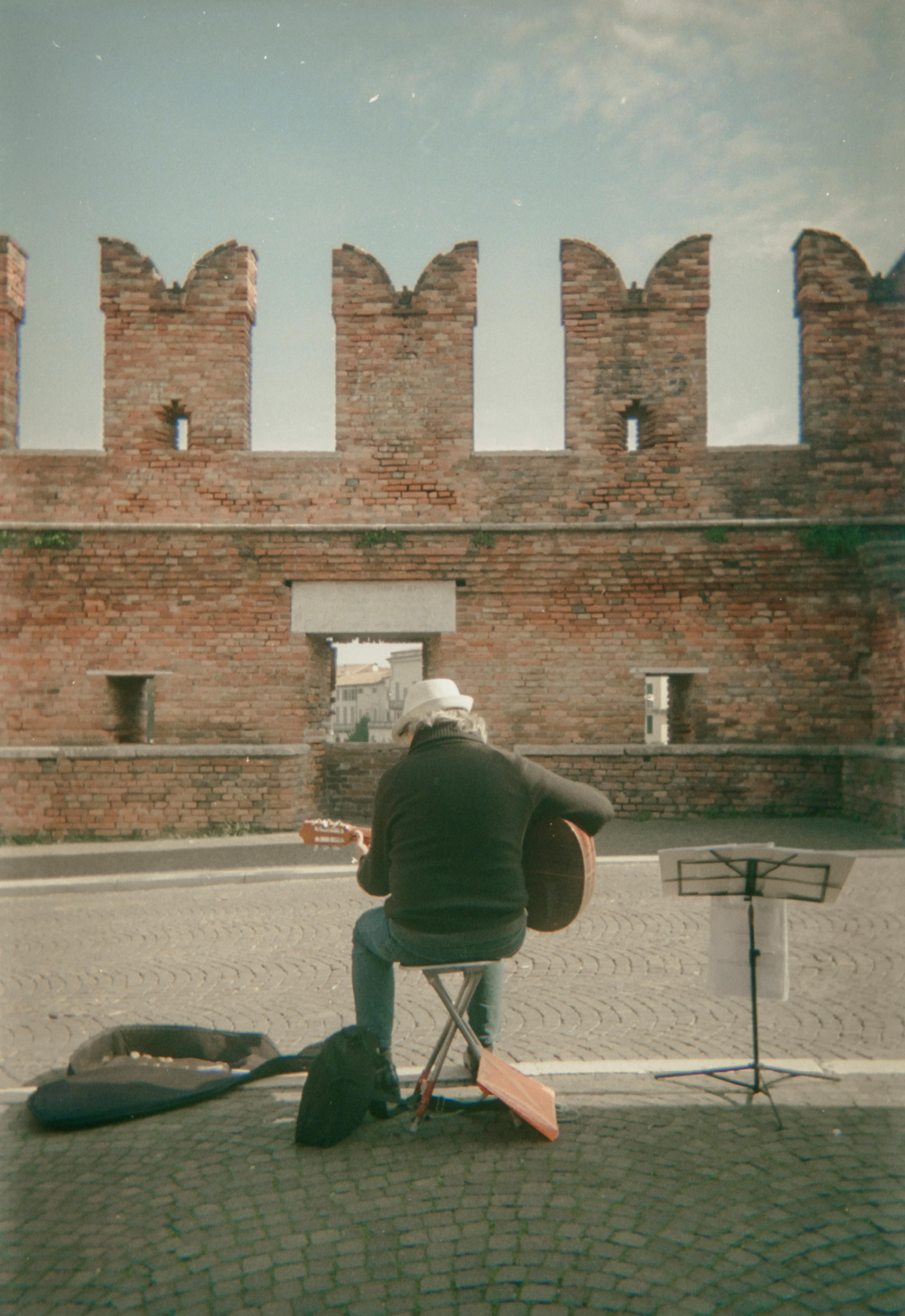 Gratis En gatemusikant opptrer med gitar nær en gammel murvegg, noe som skaper en vintage-stemning. Arkivbilde