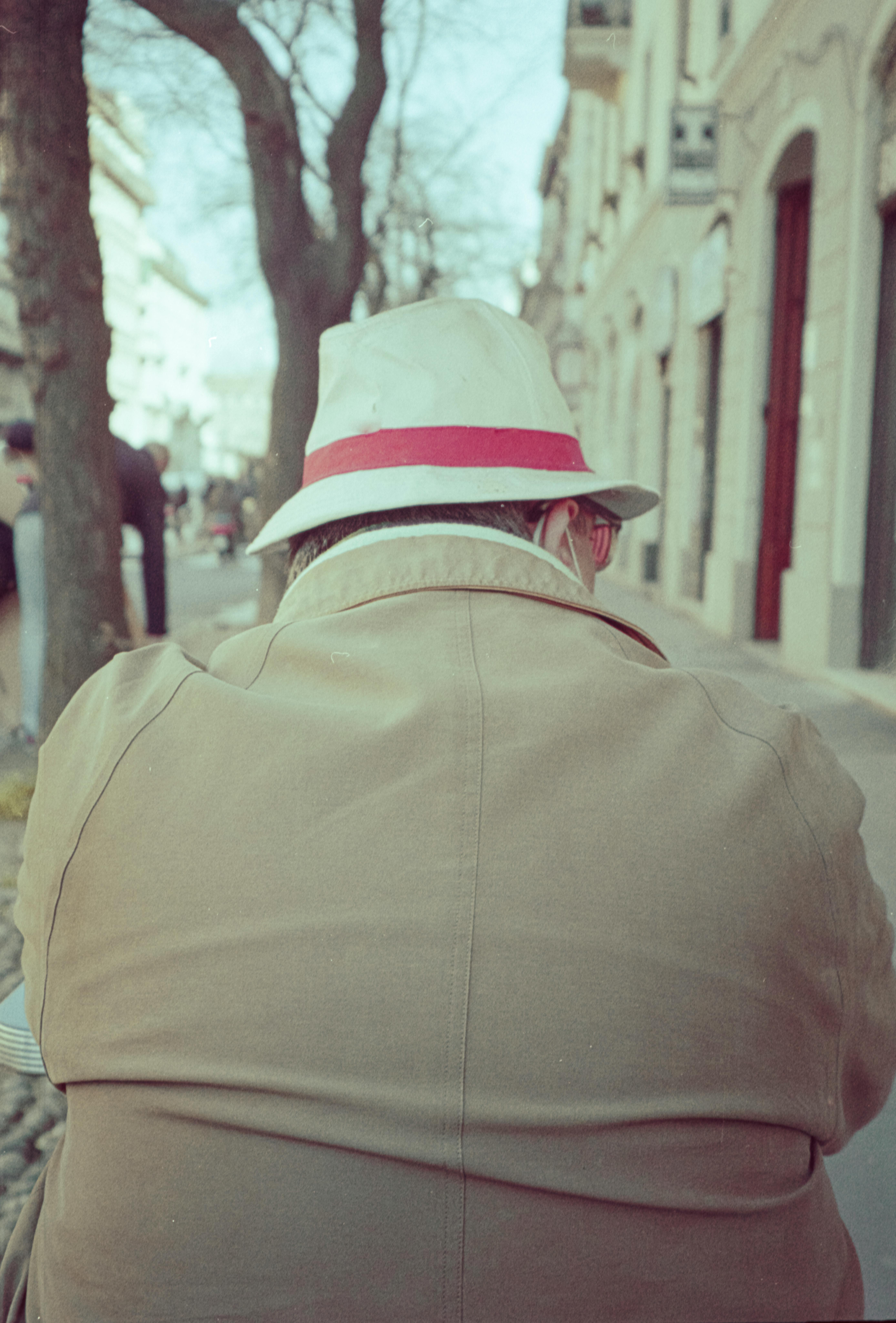 Kostnadsfria En äldre man i hatt sitter utomhus på en gata, sedd bakifrån. Stock foto
