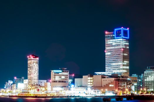 A vibrant night view of Takamatsu's cityscape in Kagawa, Japan, showcasing illuminated skyscrapers along the waterfront.
