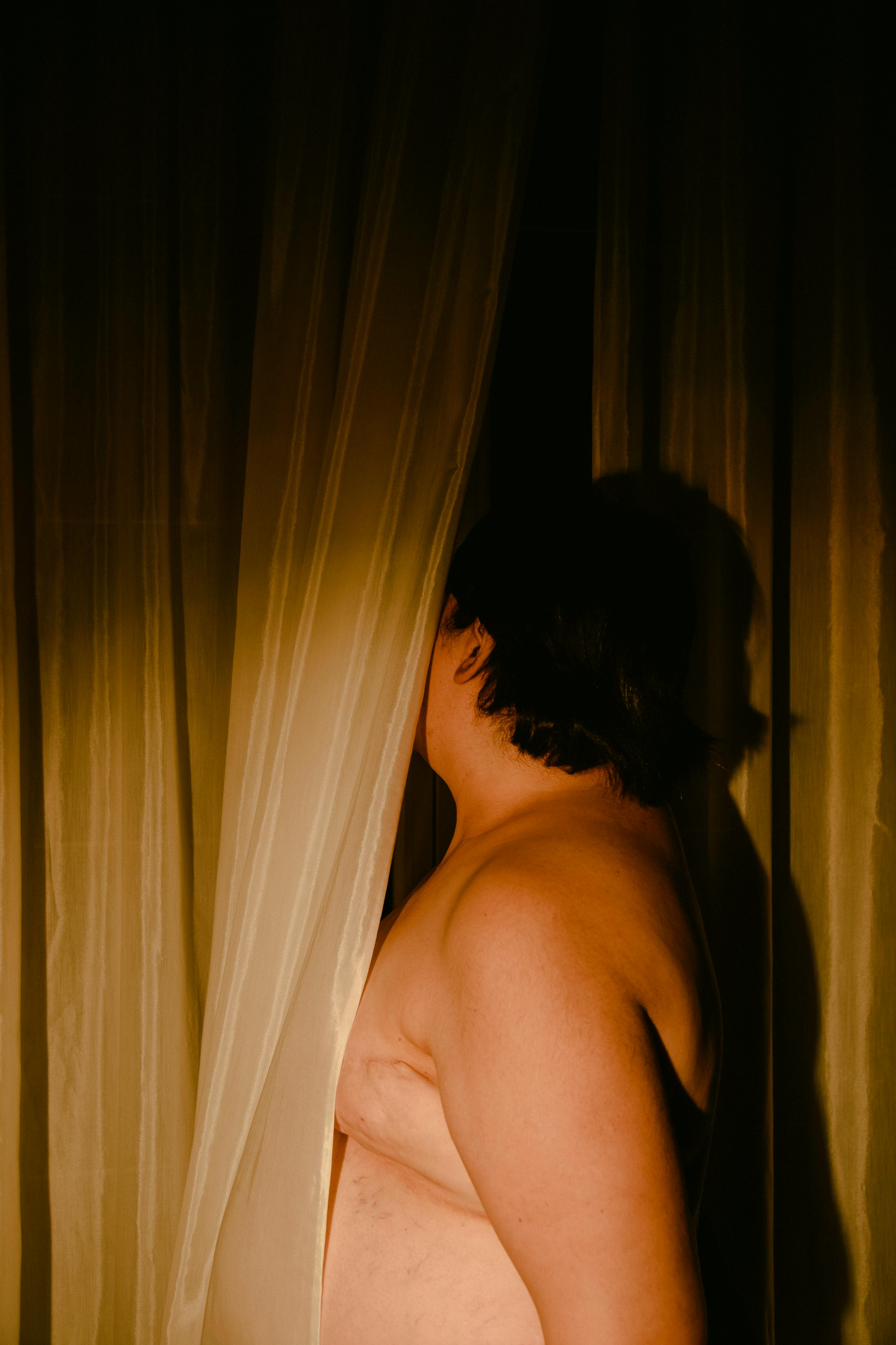 Kostenlos Künstlerische Silhouette einer Person, die teilweise hinter einem Vorhang steht, eingefangen in warmem Licht. Stock-Foto