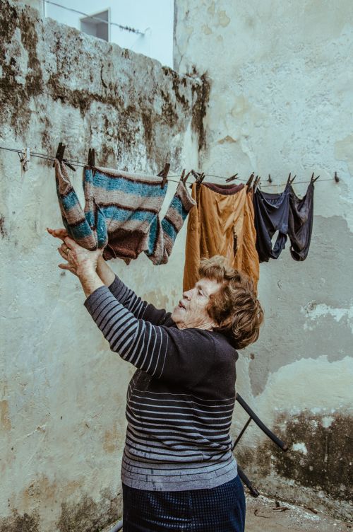 Free An elderly woman hangs clothes on an old, weathered clothesline outside. Stock Photo