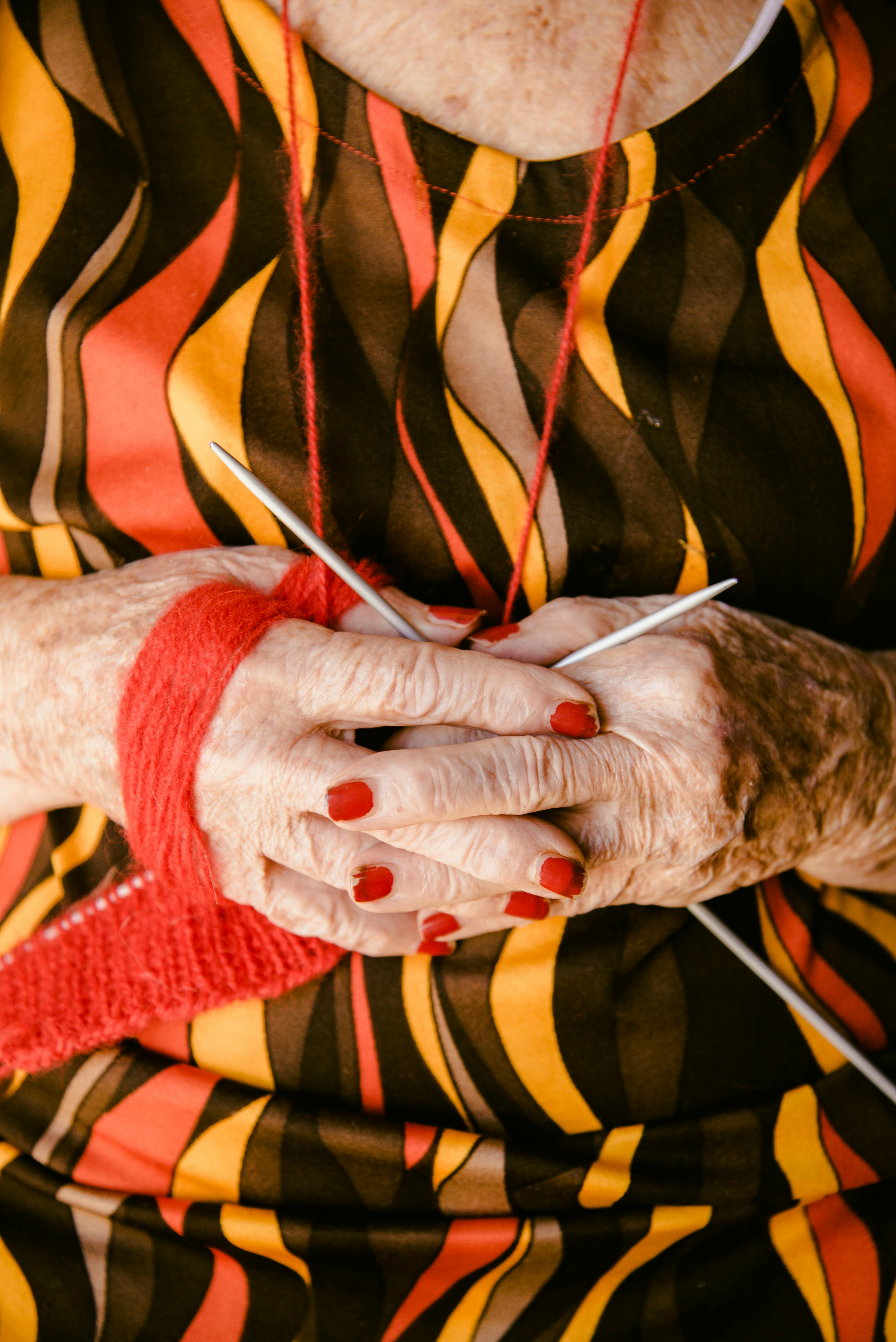 Kostenlos Nahaufnahme der Hände einer älteren Frau, die mit rotem Garn strickt und dabei Geduld und handwerkliches Geschick beweist. Stock-Foto
