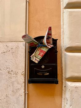 Rustic Italian mailbox with newspapers in Rome's vibrant street.