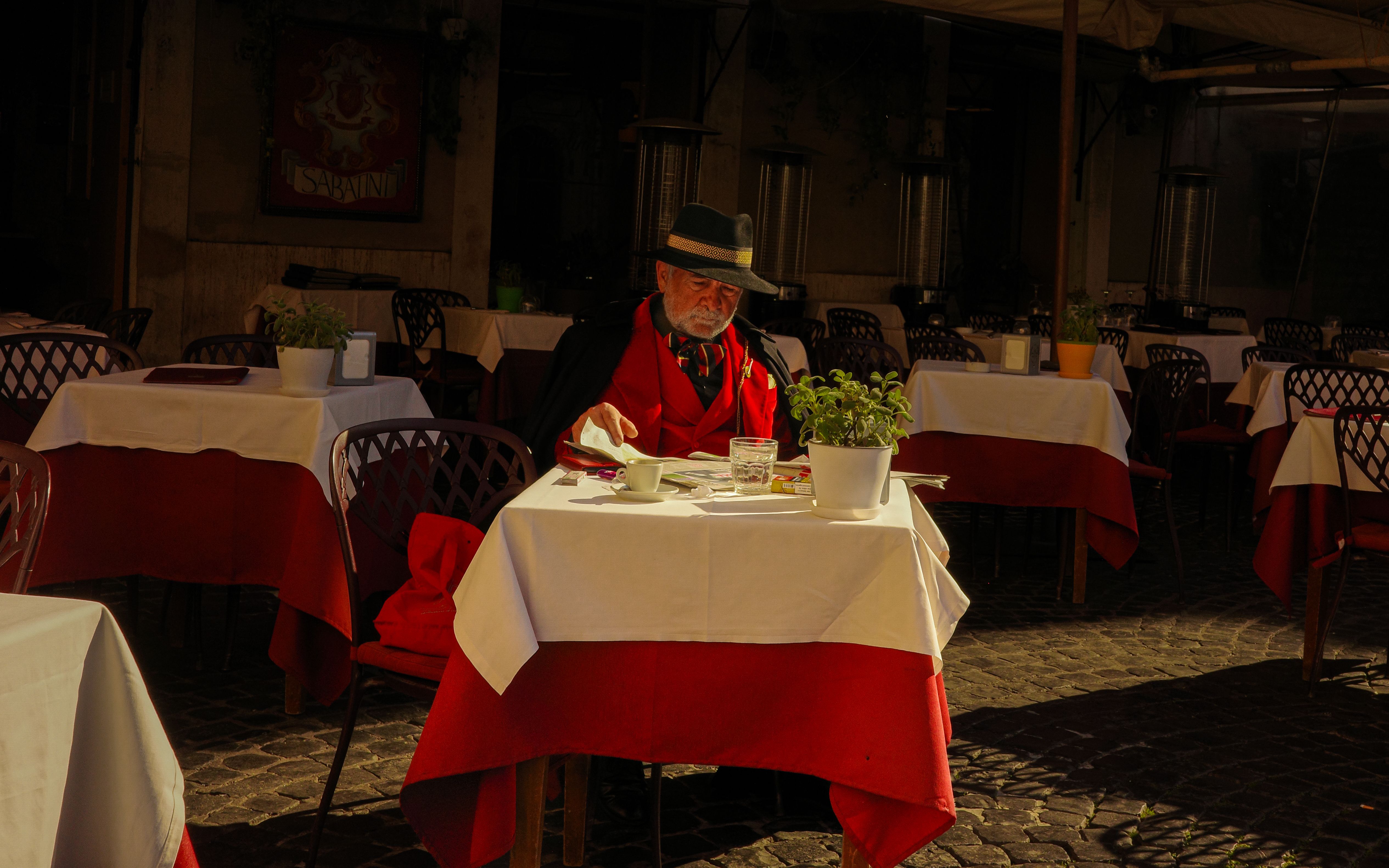 Un anziano signore si gode un pasto in un caffè all'aperto illuminato dal sole nel Lazio, in un'atmosfera incantevole.