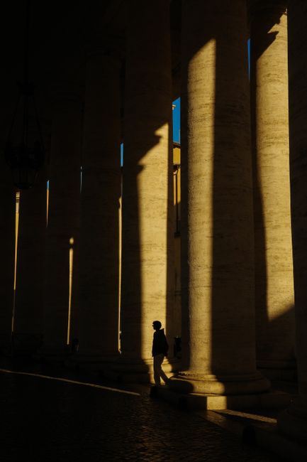 Dramatic play of light and shadow in St. Peter's Basilica. A silhouette of a person amidst grand columns in Rome, Italy.