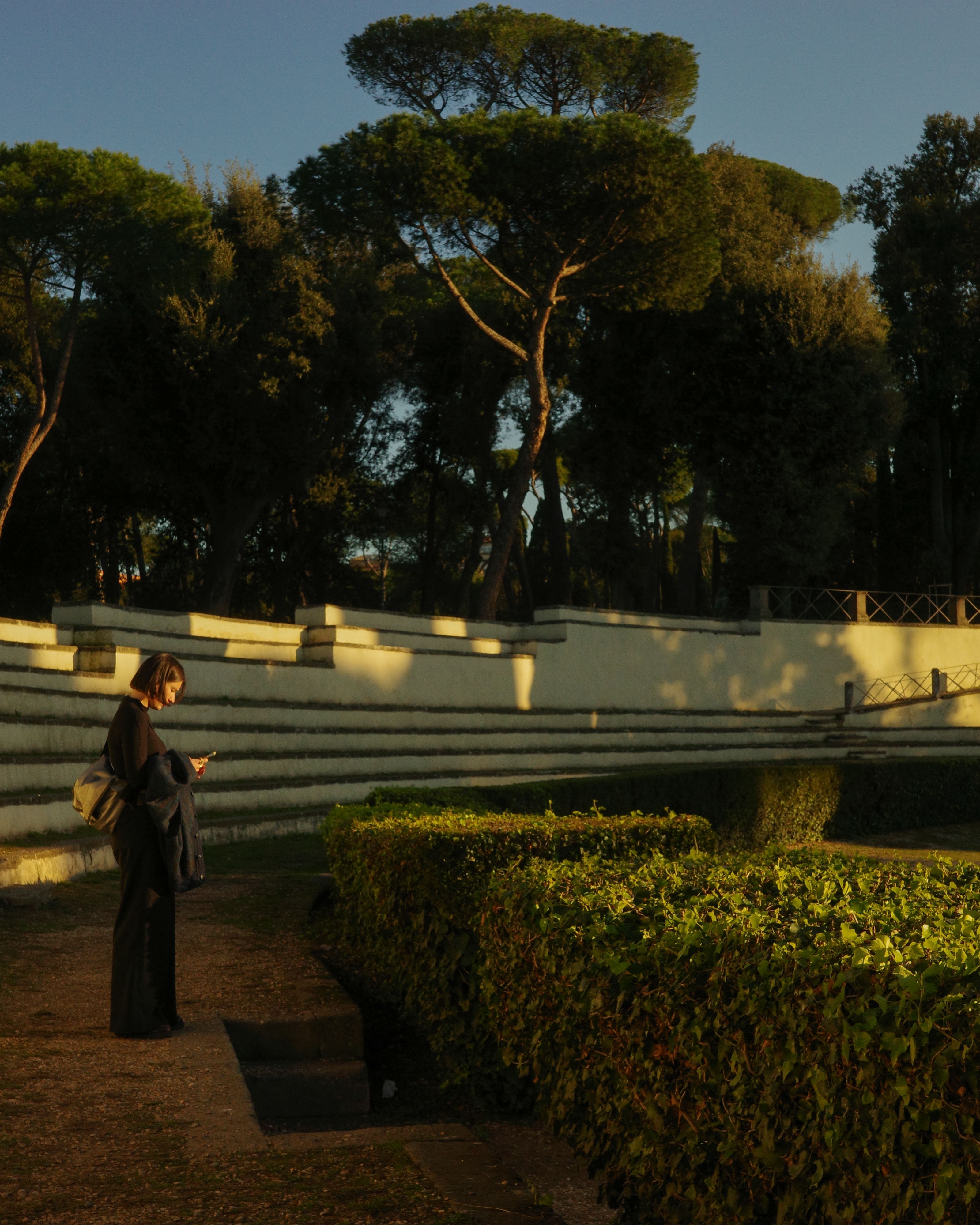 Woman walking in a tranquil Lazio park at sunset, casting long shadows.
