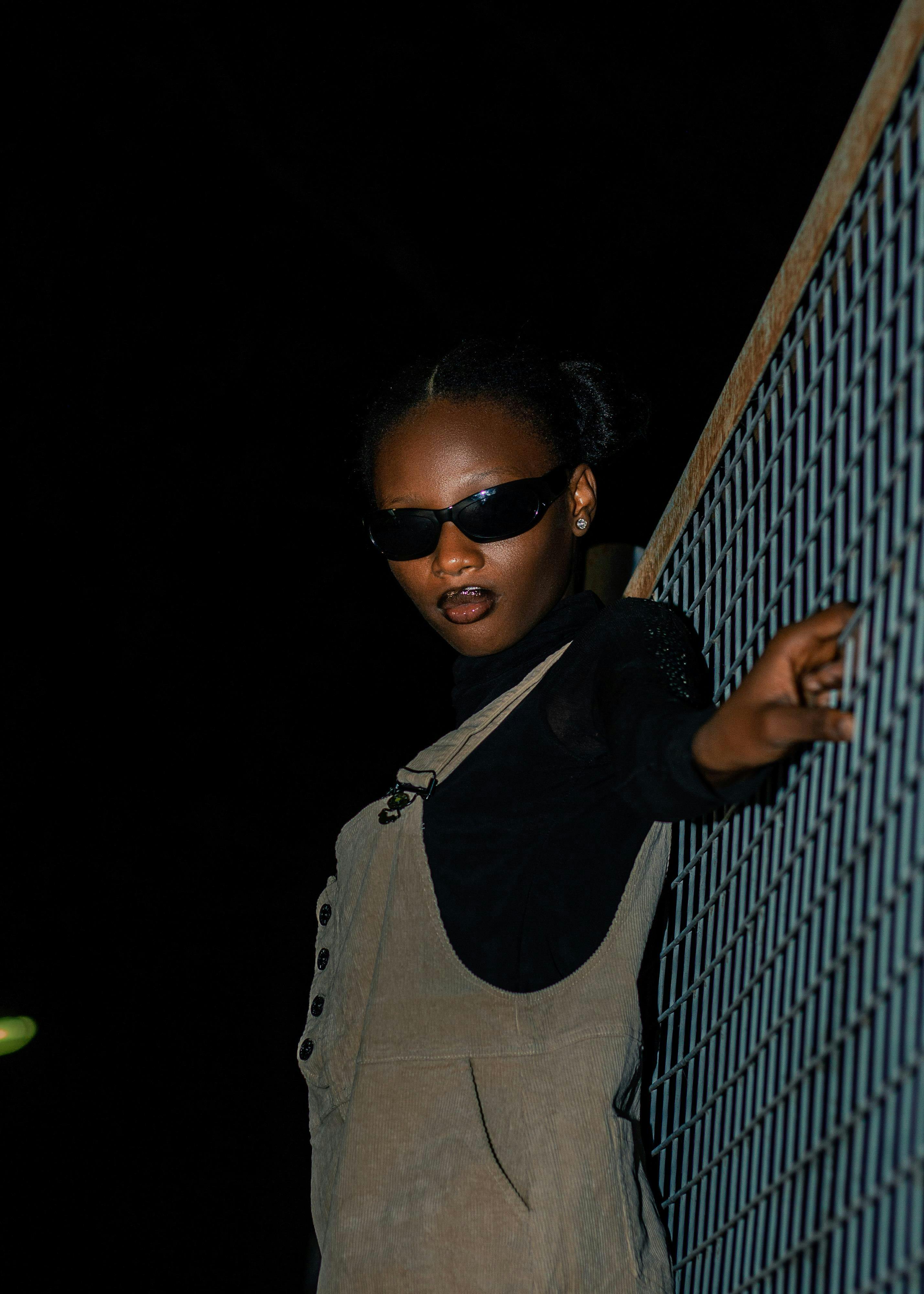 Miễn phí Người phụ nữ sành điệu đeo kính râm tựa vào hàng rào vào ban đêm, toát lên vẻ tự tin và phong cách. Ảnh lưu trữ