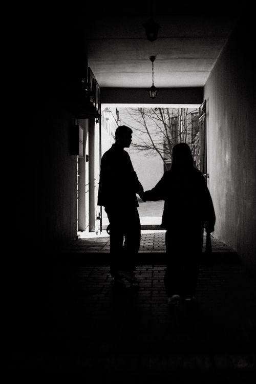 Free Moody black and white silhouette of two people walking in an alley. Stock Photo