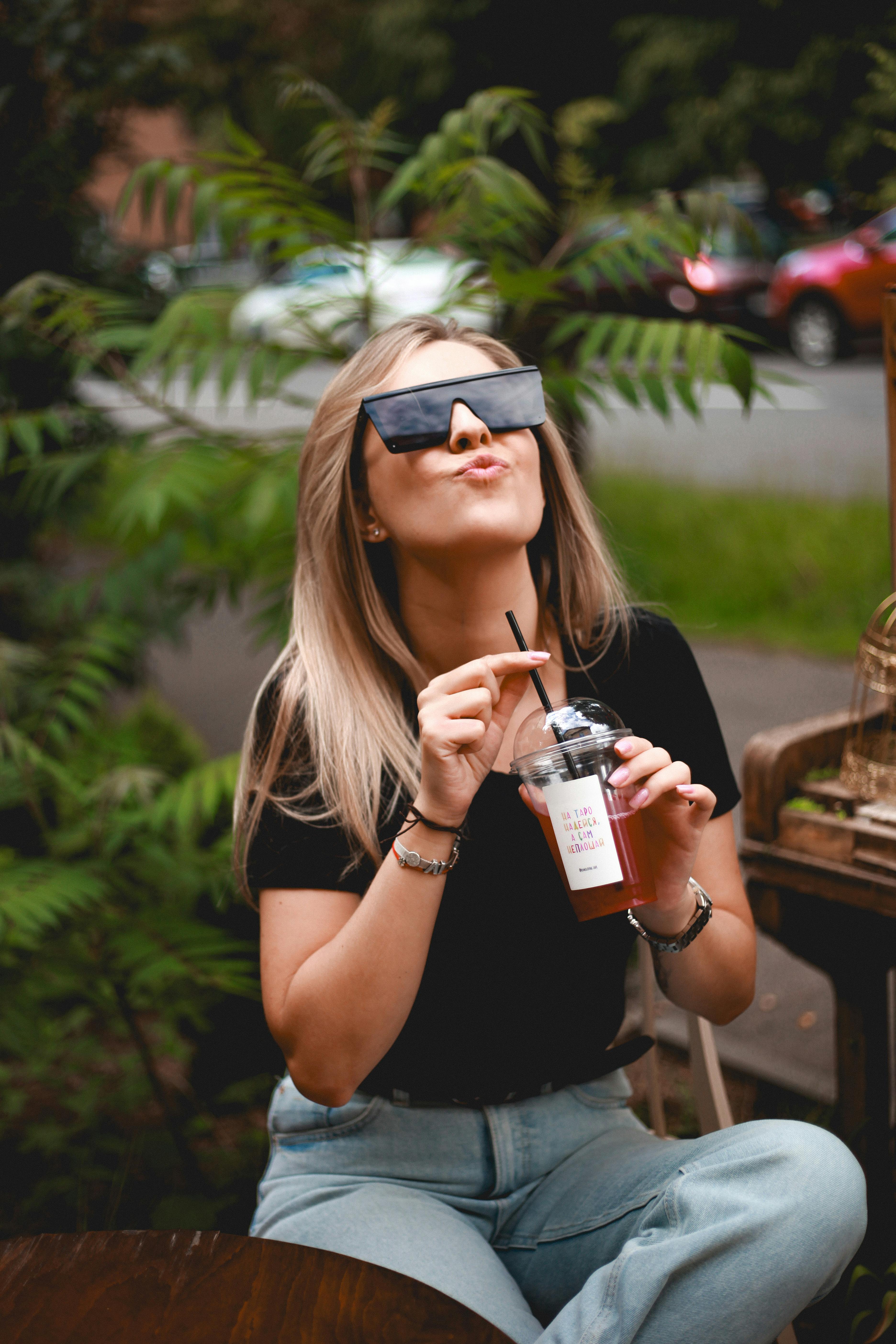 無料 おしゃれな若い女性が、夏の屋外でストローを使って飲み物を楽しんでいる。 写真素材