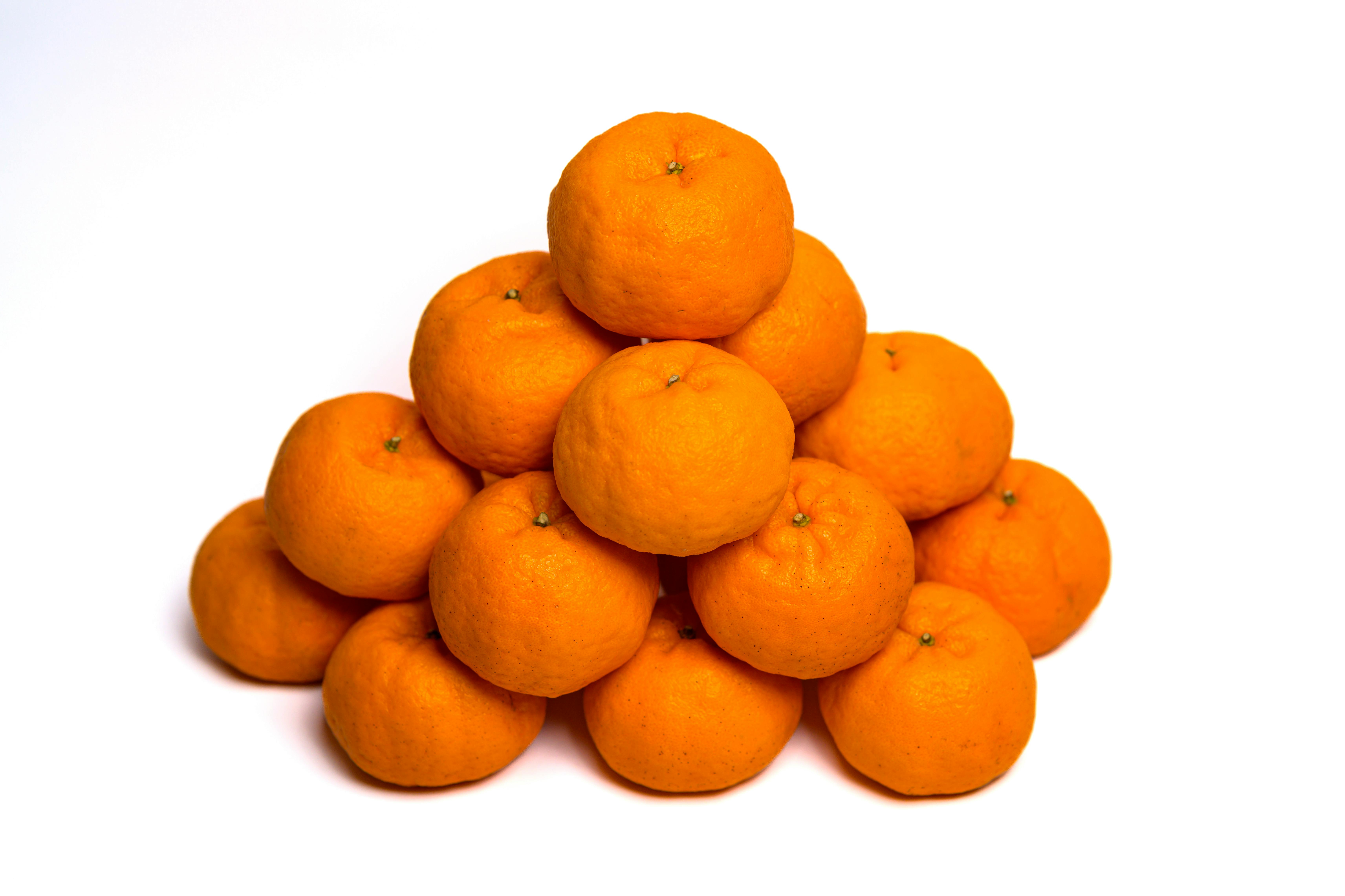 Kostenlos Eine Pyramide aus leuchtend orangefarbenen Mandarinen auf reinem weißen Hintergrund, die Frische und Schlichtheit symbolisiert. Stock-Foto