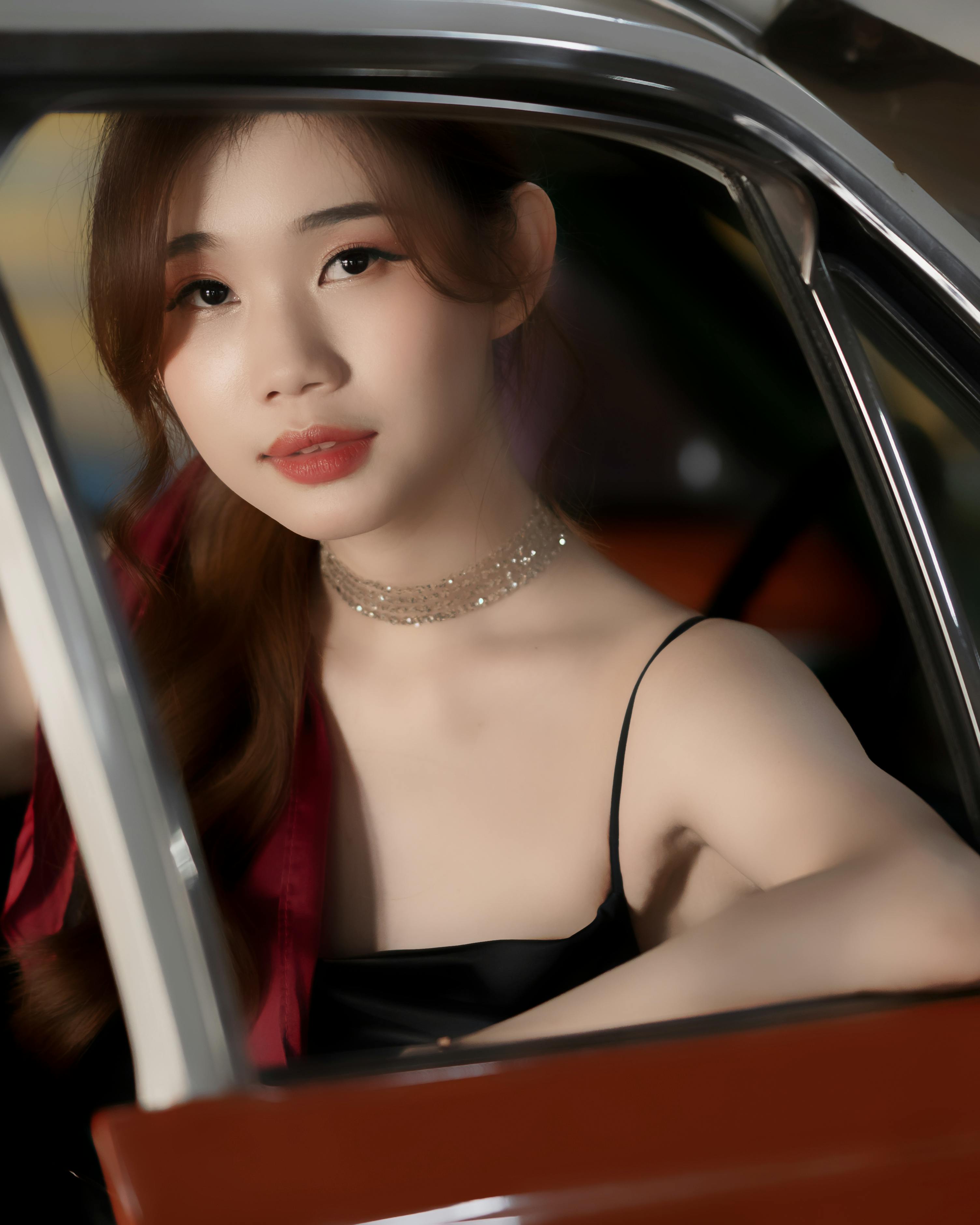 grátis Uma jovem elegante posando dentro de um carro antigo, capturando uma atmosfera sofisticada e atemporal. Foto profissional