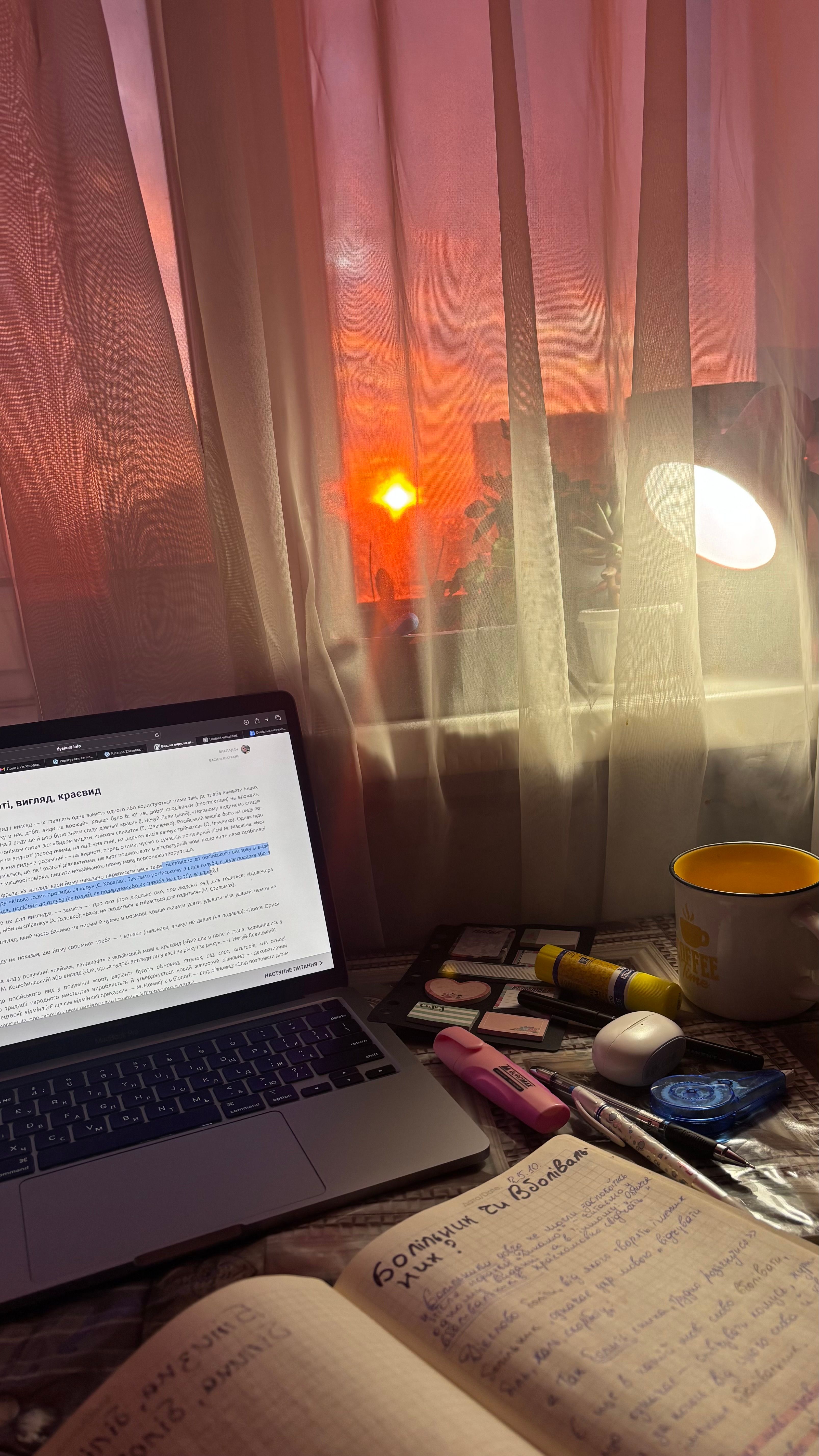 A warm, inviting study setup by the window with a glowing sunset, laptop, and notebooks, perfect for inspiration.