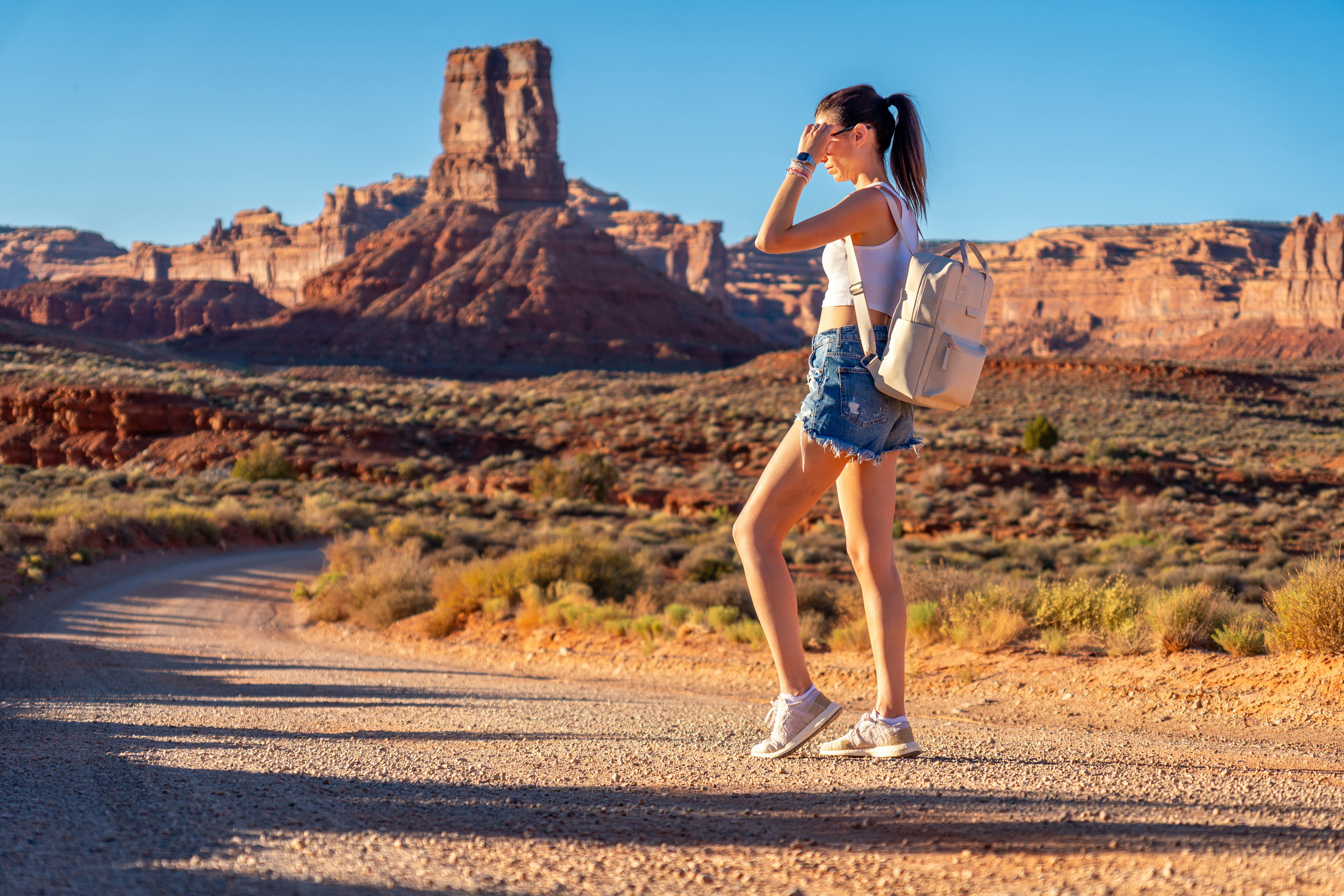 無料 澄み切った青空の下、ユタ州の砂漠地帯をハイキングする若い女性。そこには象徴的な岩層が点在している。 写真素材