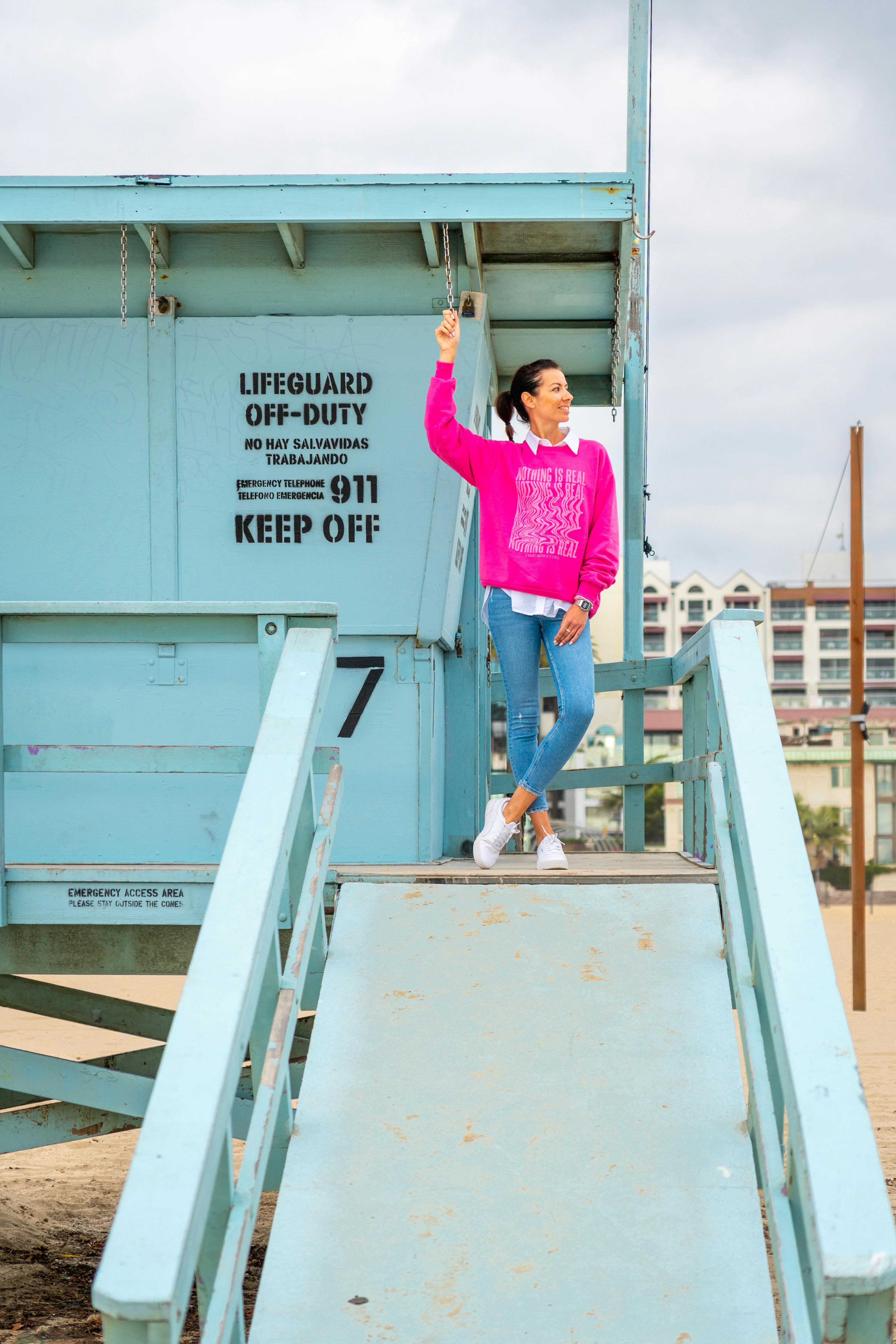 無料 サンタモニカのライフガードタワーのそばでポーズをとる女性。ビーチファッションと活気に満ちたライフスタイルを披露している。 写真素材