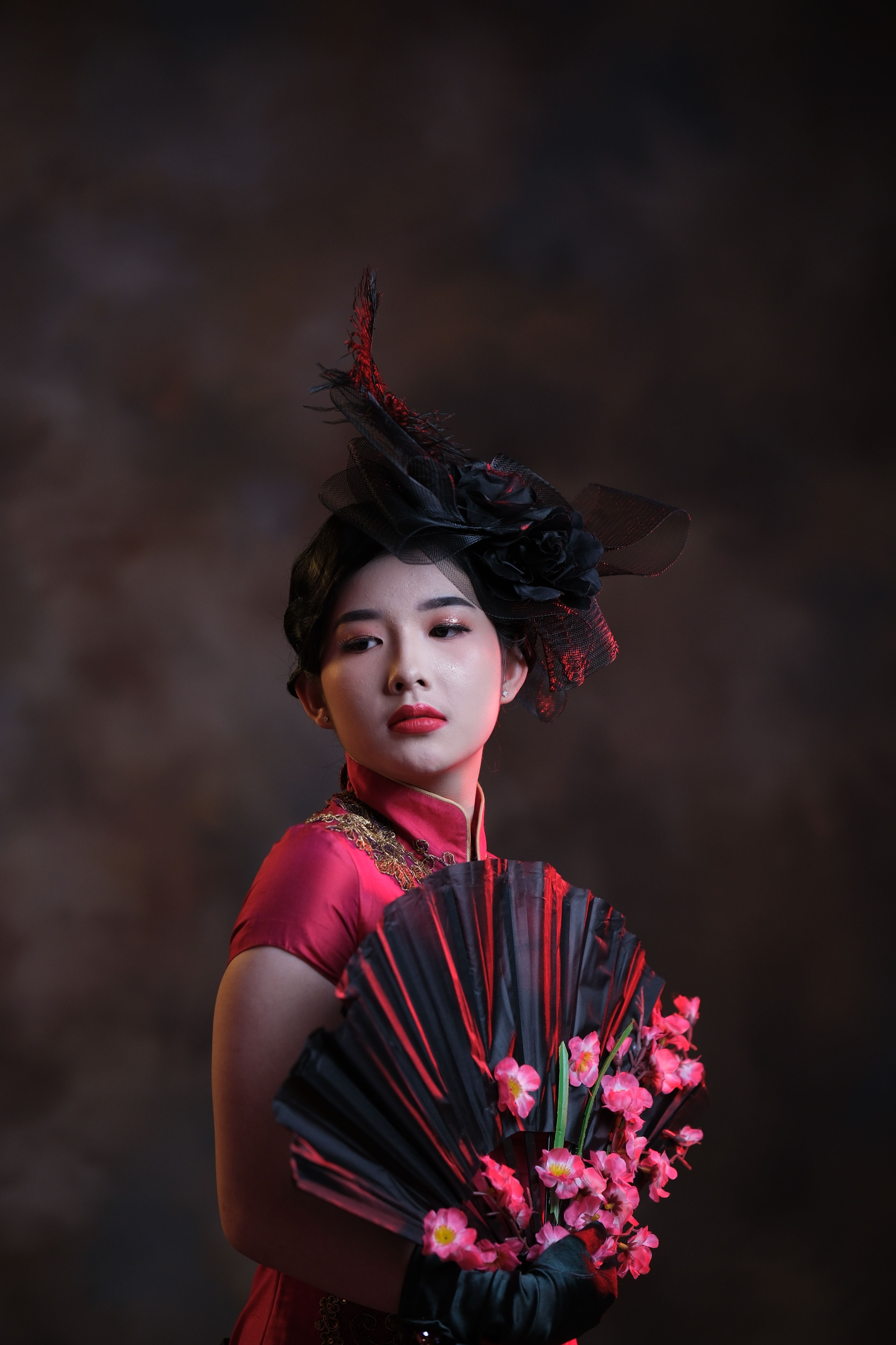 A sophisticated woman in red attire posing gracefully with an oriental fan, exuding elegance and style.