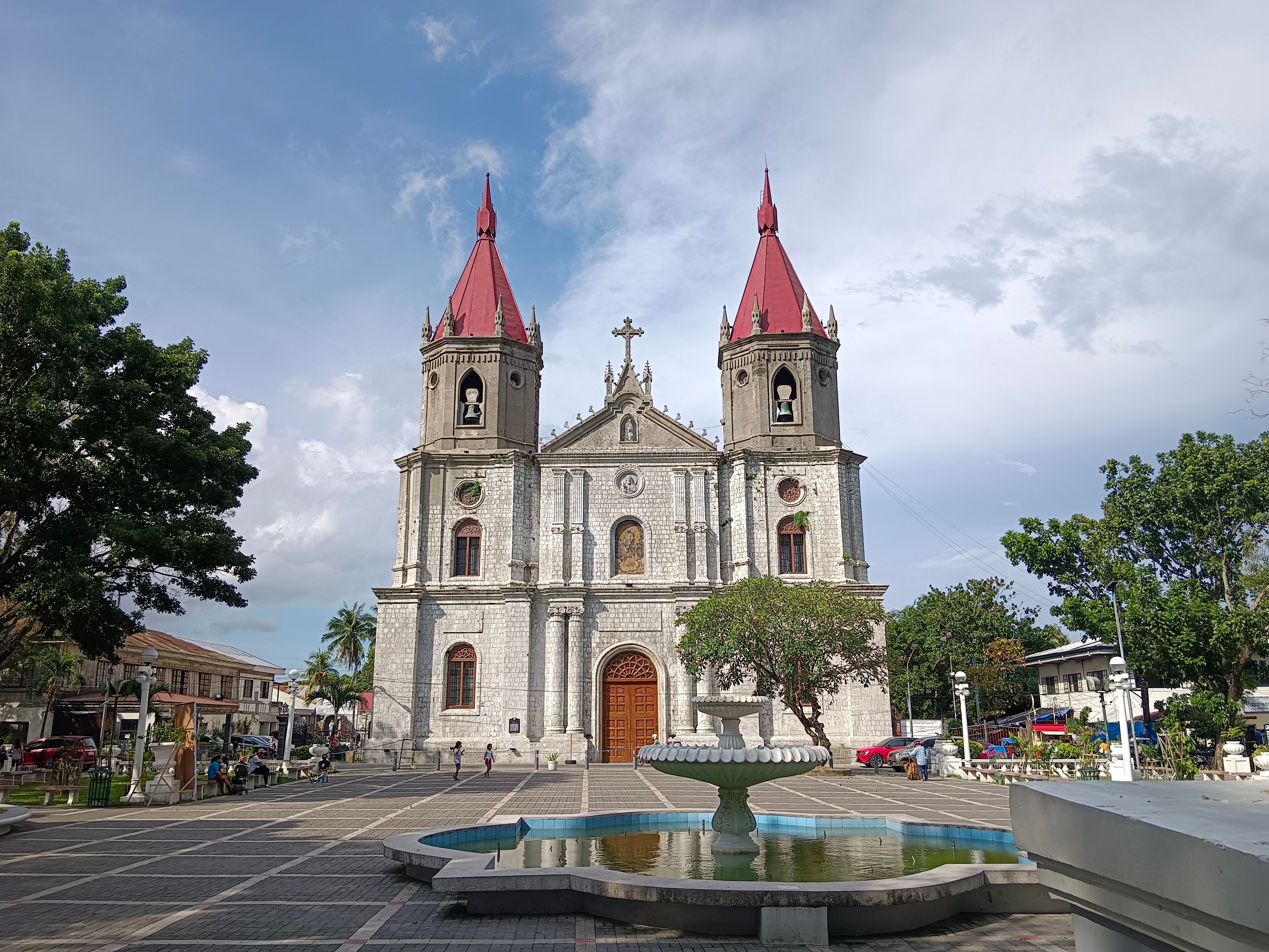 A beautiful colonial-style church stands with towering red spires and a serene fountain in the foreground.