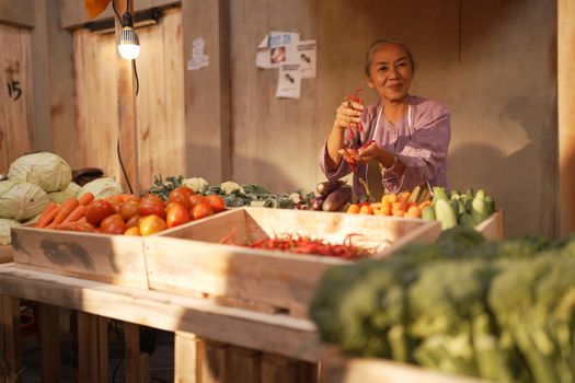 Elderly woman showcasing fresh vegetables at a bustling outdoor market stand.