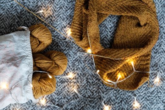 Warm knitted scarf with yarn balls and holiday lights on a textured carpet, evoking a cozy winter vibe.