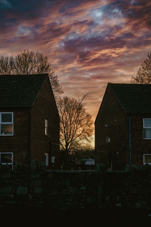 Free A stunning sunset with vibrant clouds between two brick houses, creating a dramatic silhouette. Stock Photo