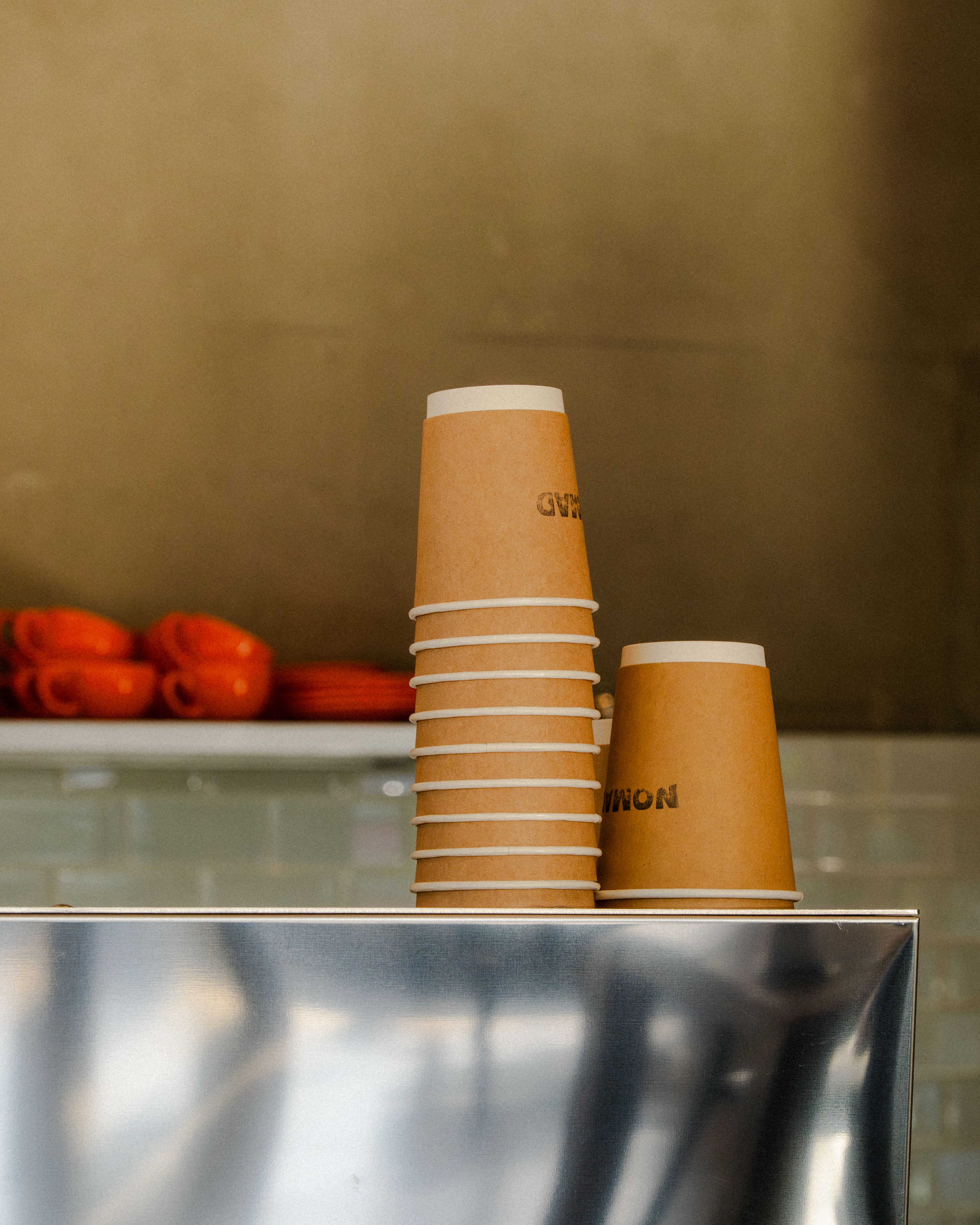 A stack of brown paper coffee cups in a minimalist cafe with a stainless steel counter.