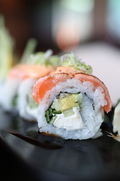 Free Close-up of a salmon sushi roll with fresh ingredients on a black plate. Stock Photo