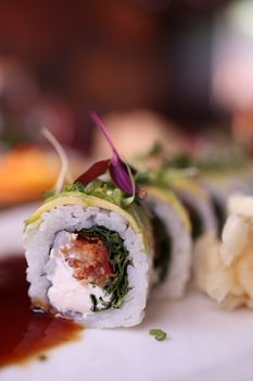 Sushi roll with cream cheese, nori, and microgreens, beautifully garnished on a white plate.
