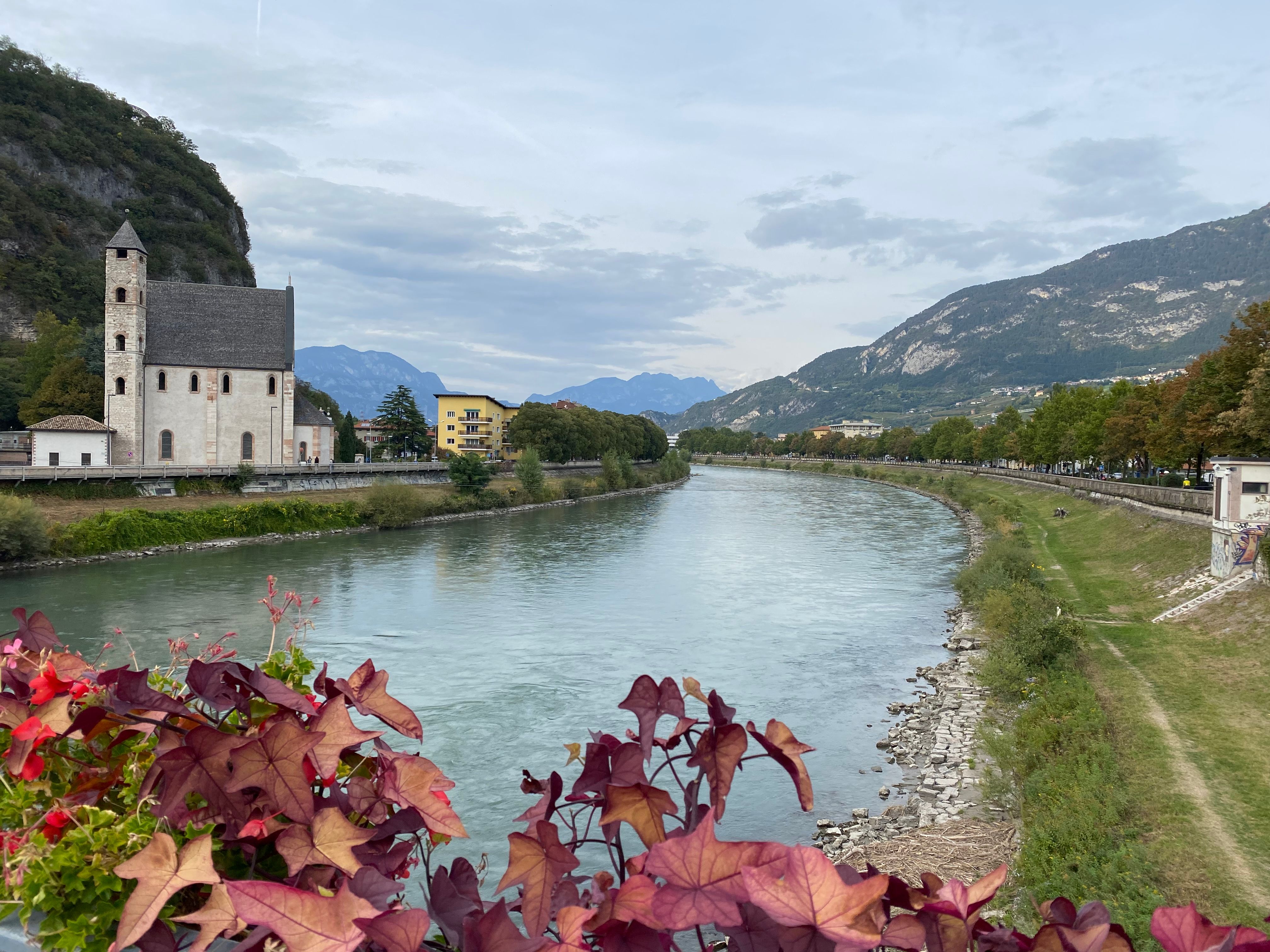 Scenic view of a historic church by the river in Trento, Trentino-Alto Adige, Italy. Captured in a serene outdoor setting.