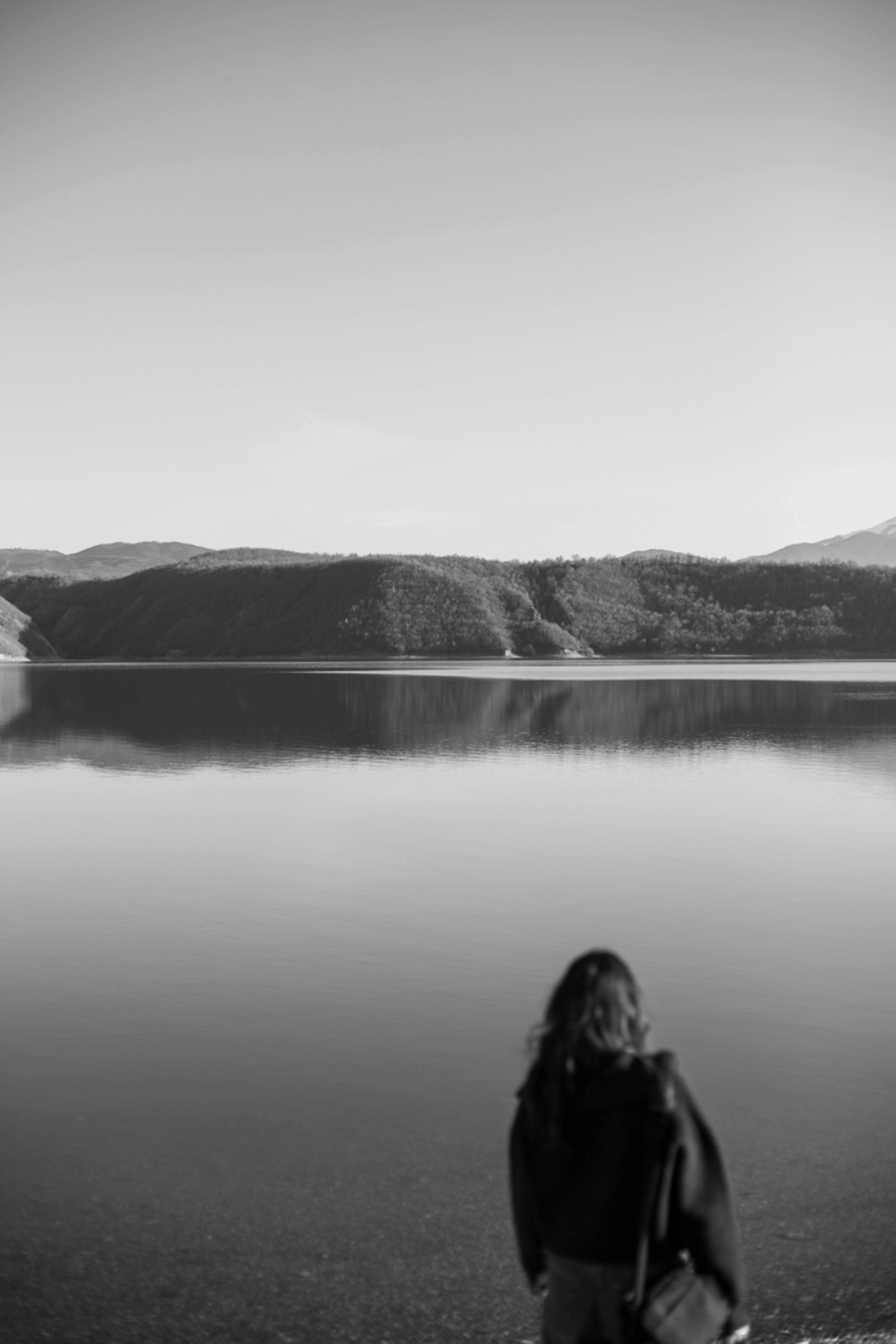 Zadarmo Žena stojí pri pokojnom jazere, obklopená vzdialenými kopcami, a vytvára tak pokojnú a vyrovnanú atmosféru. Fotka z fotobanky