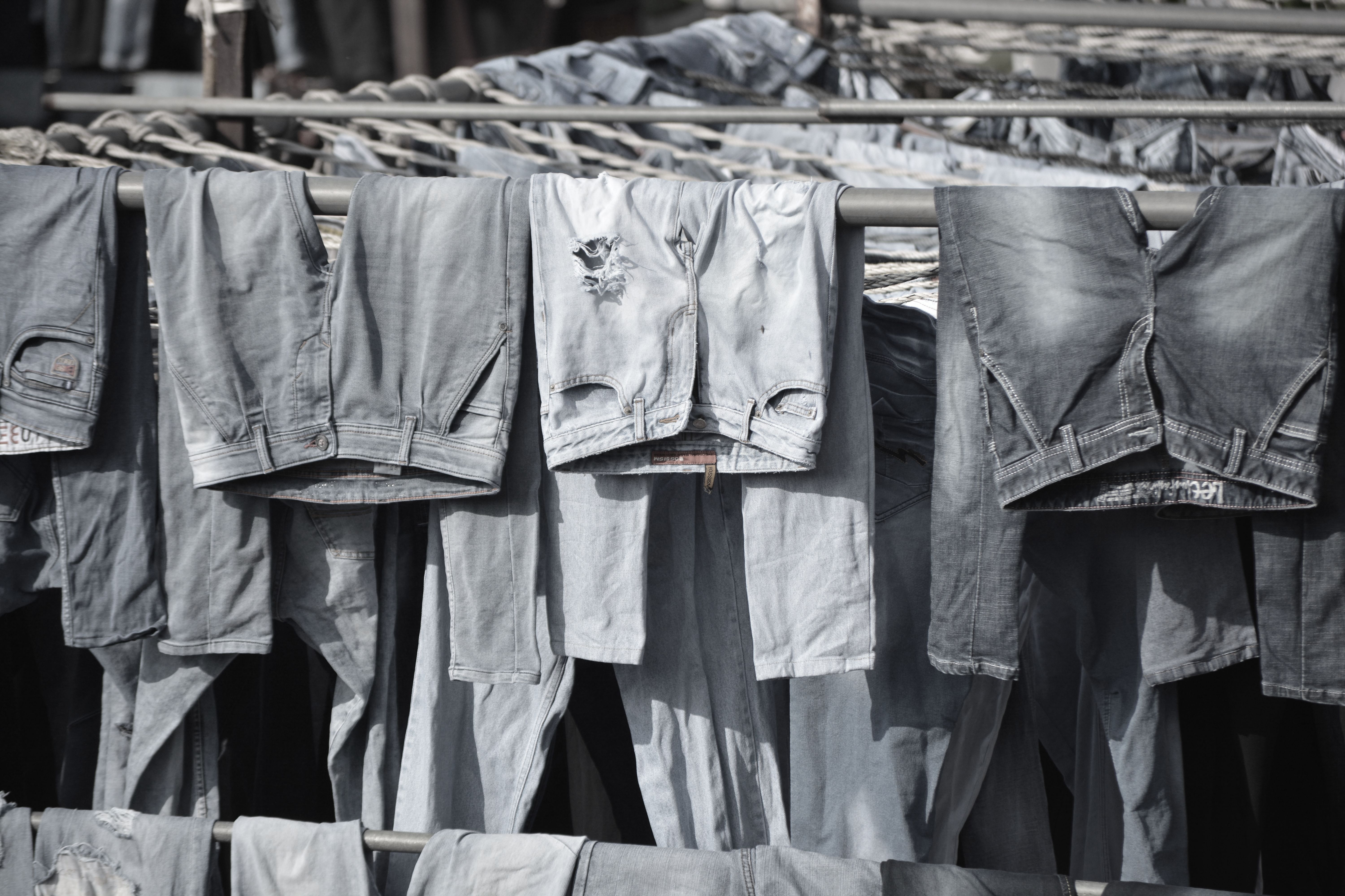 A collection of worn denim jeans hanging to dry on outdoor racks, creating a rustic and vintage vibe.