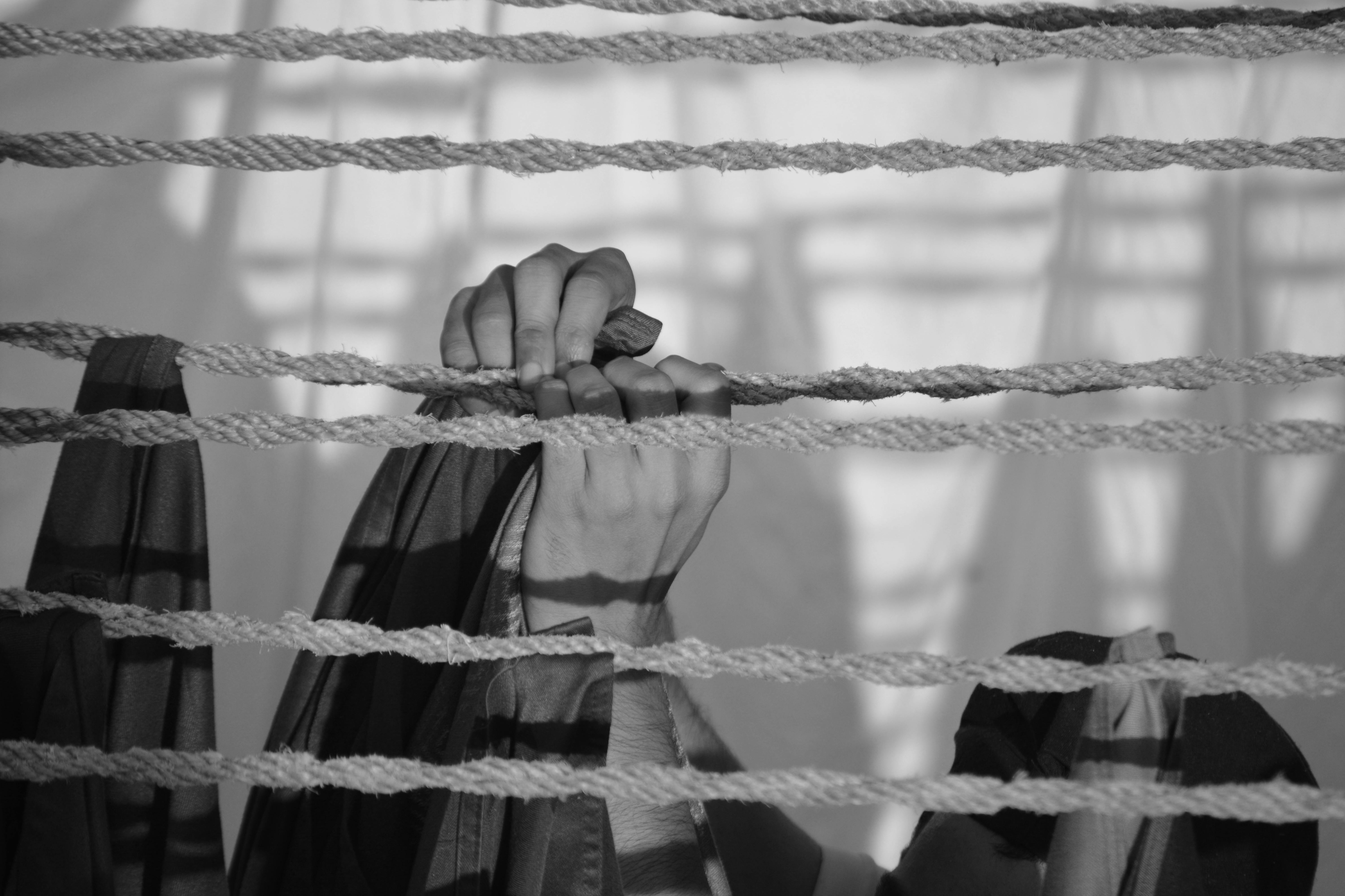 Free Monochrome image of hands clutching ropes, casting shadows, creating a dramatic effect. Stock Photo