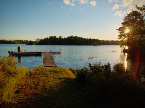 Free Peaceful lakeside view with a wooden dock, vibrant sunset, and lush trees in Pennsylvania. Stock Photo