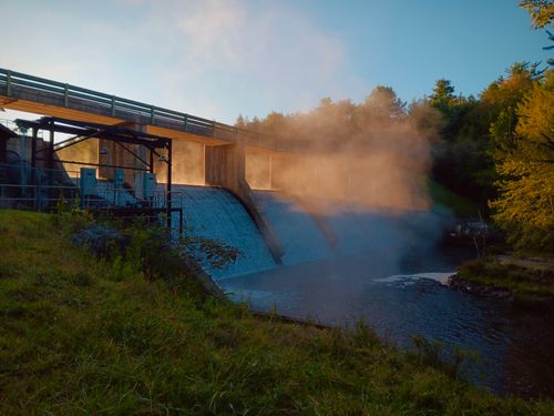 Free A dam emitting mist at sunrise, surrounded by vibrant autumn foliage in a serene outdoor setting. Stock Photo