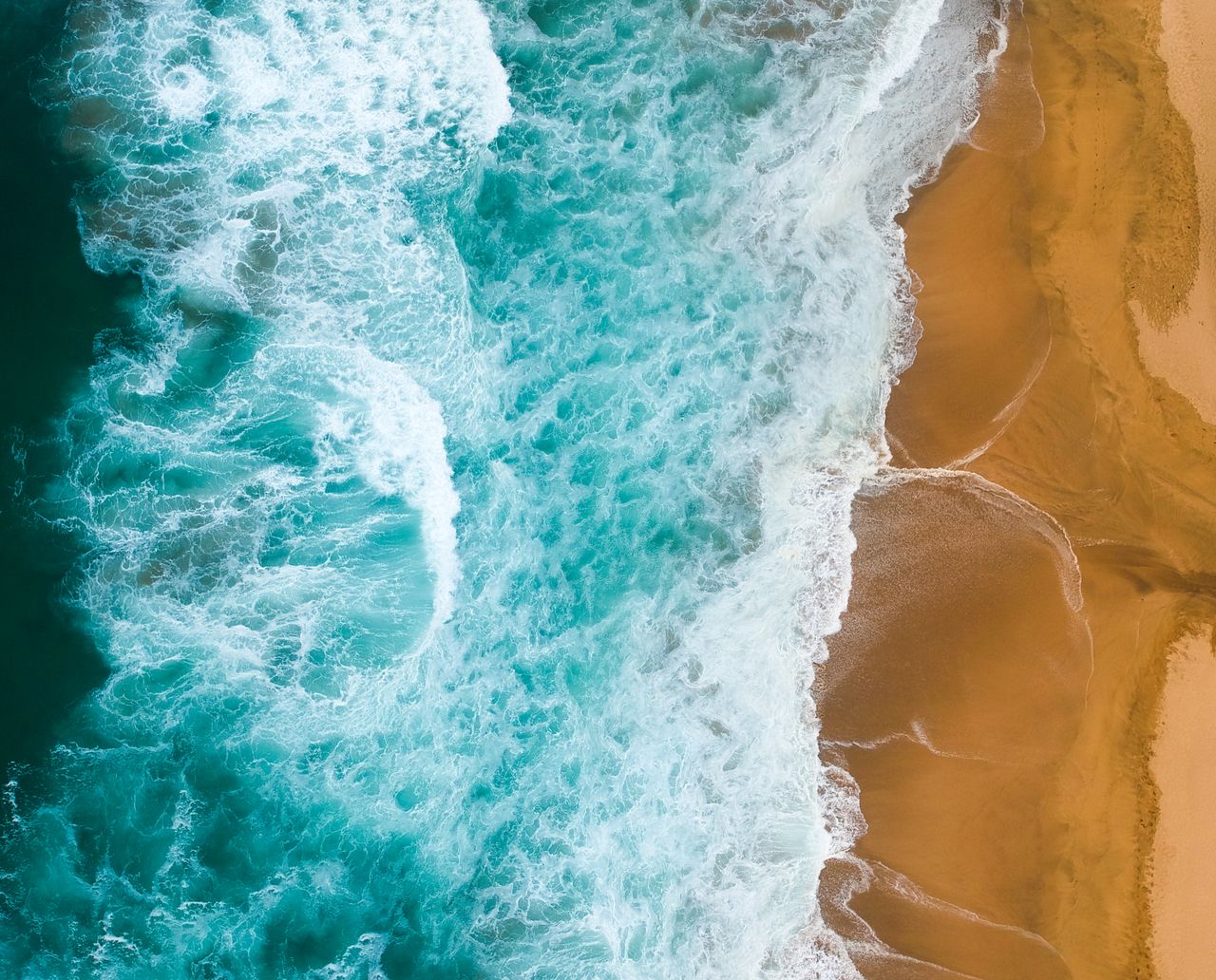 drone shot capturing turquoise waves crashing onto a golden sandy coas