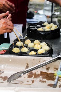 Takoyaki balls cooking on a street vendor's grill at an outdoor market.