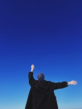 A person in black clothing stretches arms towards a vibrant blue sky, symbolizing freedom and joy.