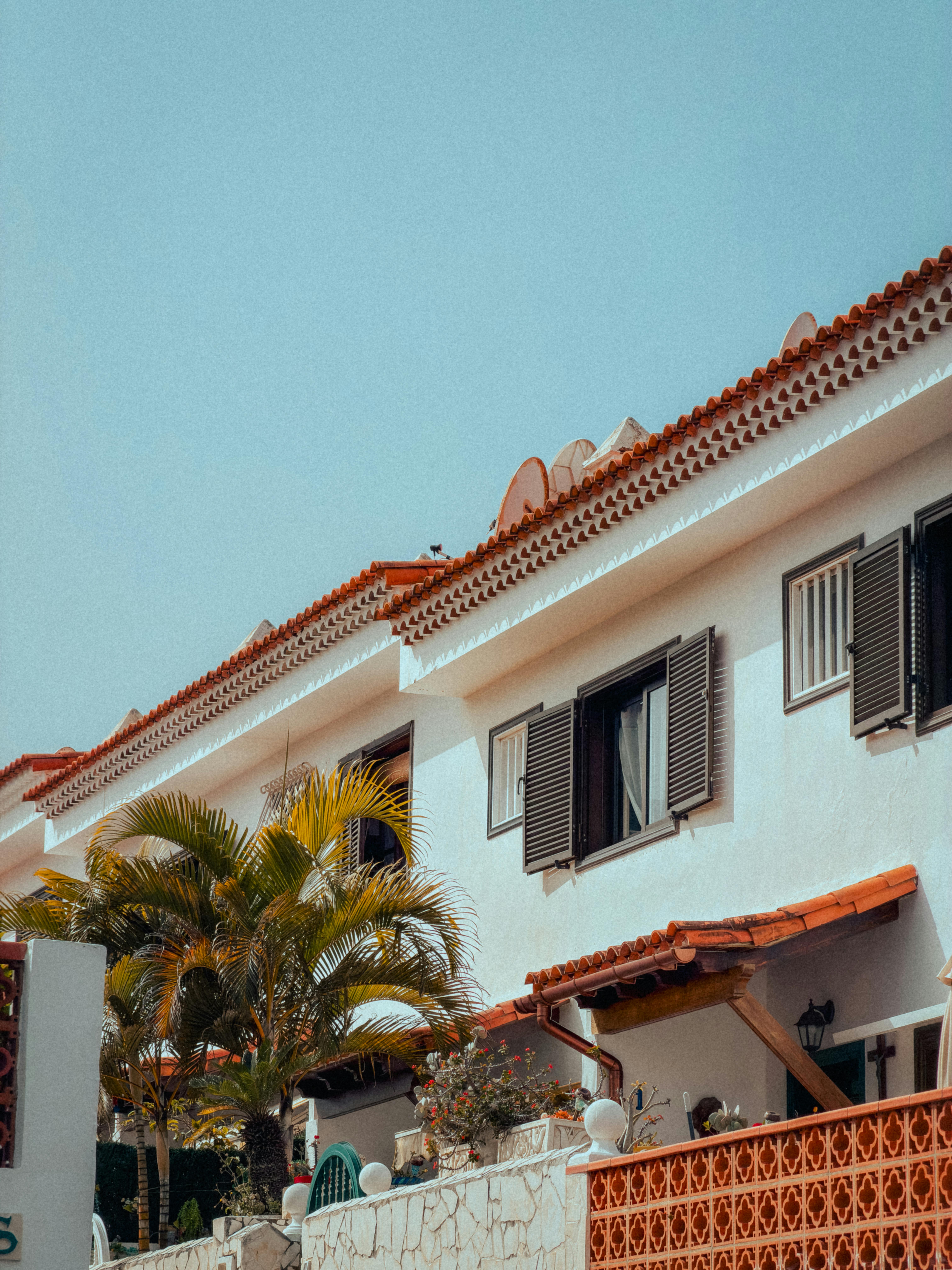 grátis Charmoso edifício em estilo colonial espanhol com telhados de terracota e palmeiras sob um céu claro. Foto profissional