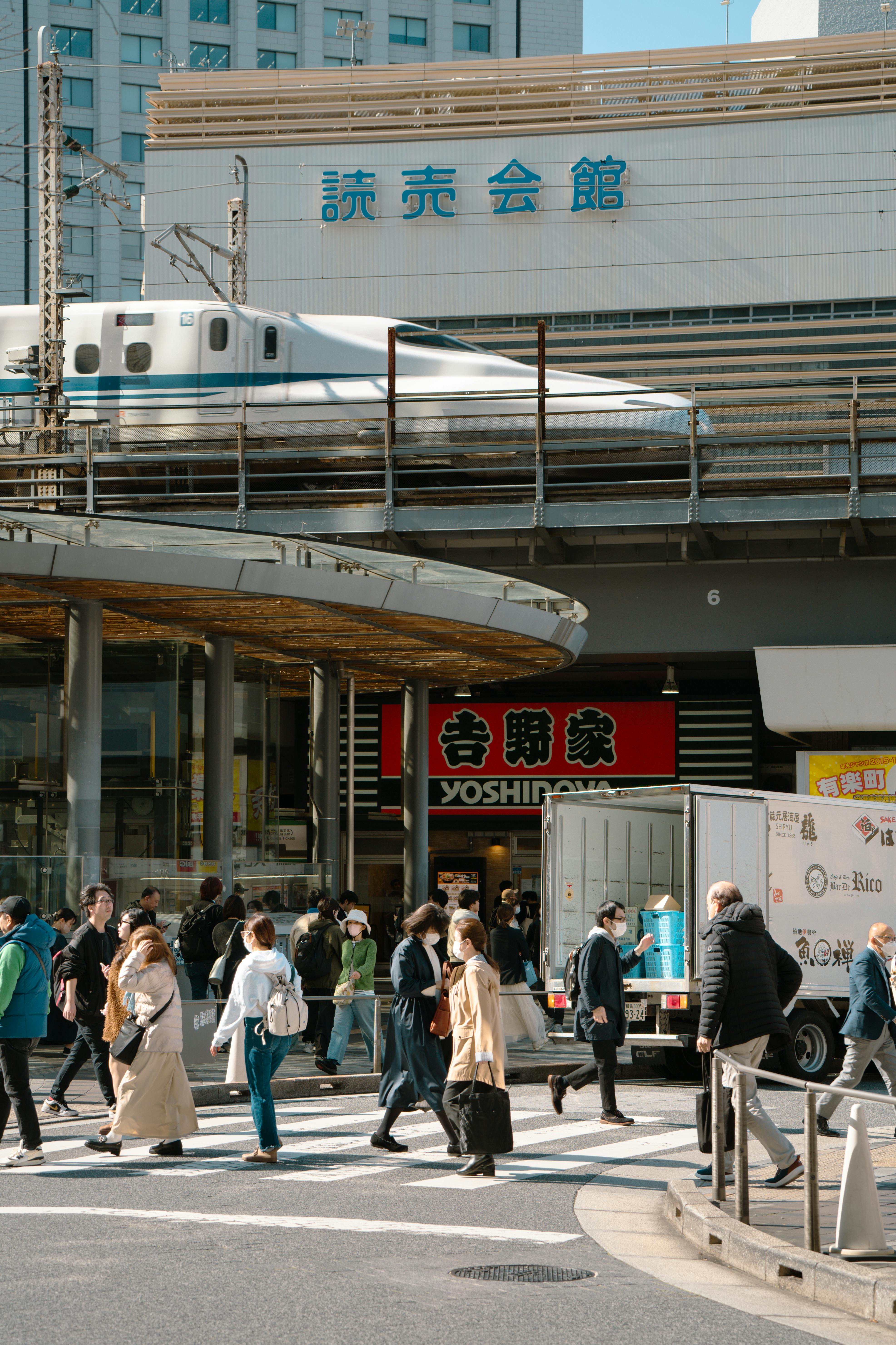 De franc La gent creua un carrer bulliciós de Tòquio mentre un tren Shinkansen passa per sobre. Entorn urbà vibrant del Japó. Foto d'estoc