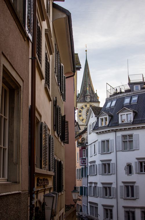 Free Explore a picturesque alley in Zurich with a view of the iconic St. Peter's Church clock tower. Stock Photo