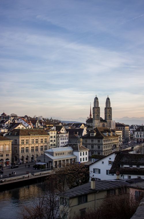 Free A picturesque view of Zurich featuring the iconic Grossmünster church at sunset over the Limmat River. Stock Photo