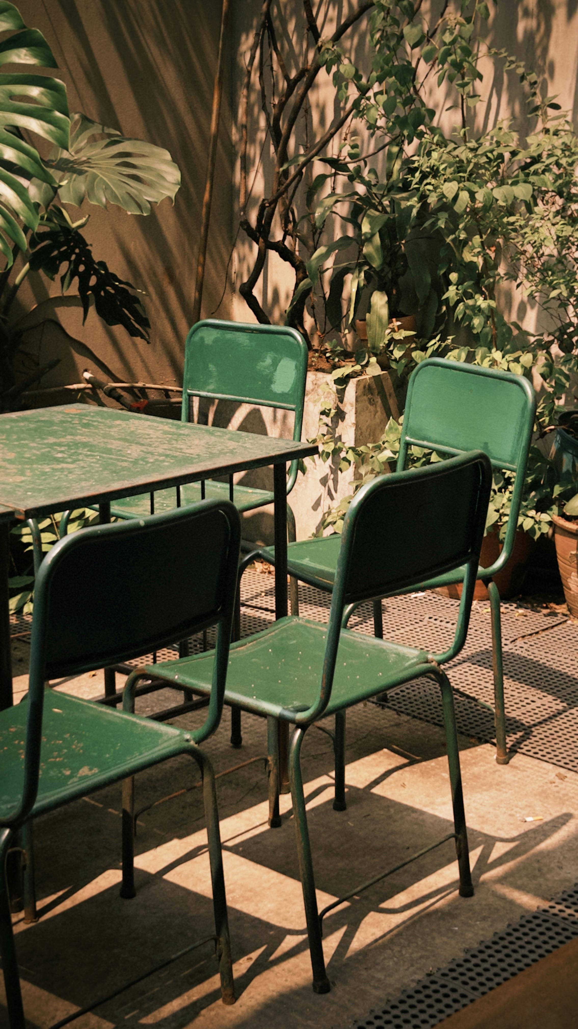 Gratis Sedie e tavolo vintage verdi, immersi nella luce soffusa del sole in un caffè all'aperto. Foto a disposizione