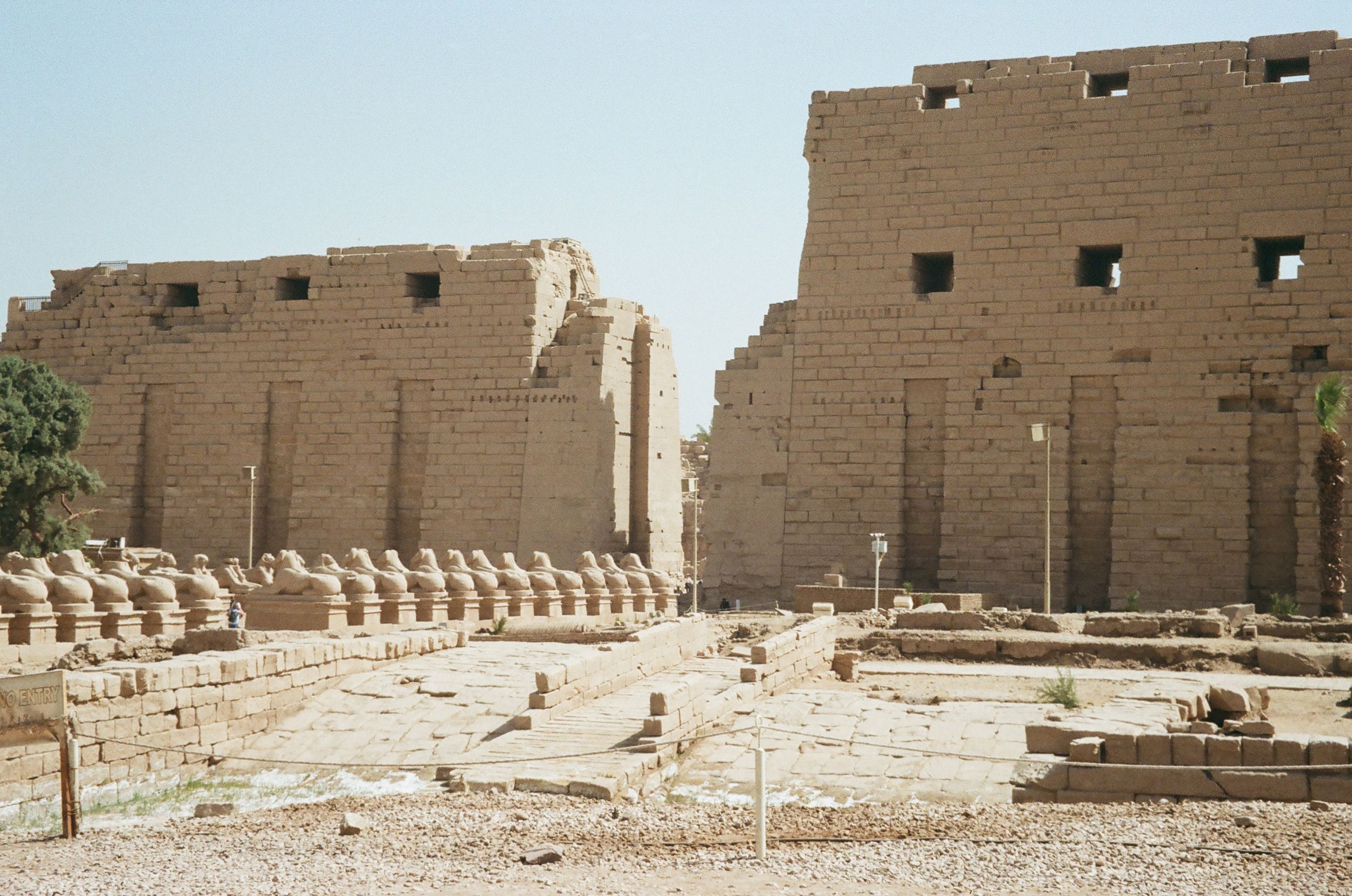 Karnak Temple pylons and ram-headed sphinxes in Luxor, Egypt, with visitors under bright desert sunlight