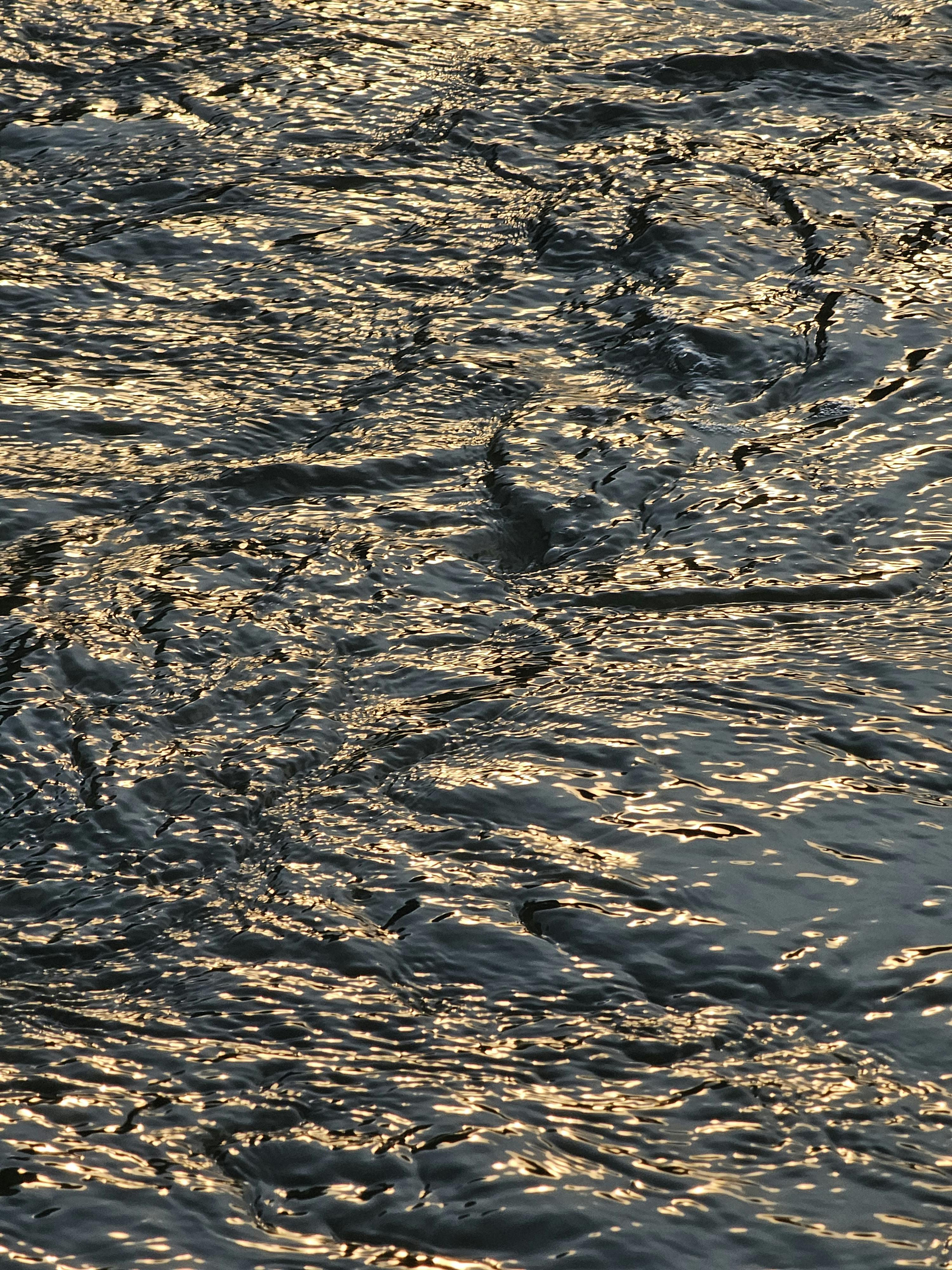 Ücretsiz Dalgalanan suyun sıcak gün batımı ışığını yansıtarak yarattığı sakin, altın rengi görünümün yakın çekim görüntüsü. Stok Fotoğraflar